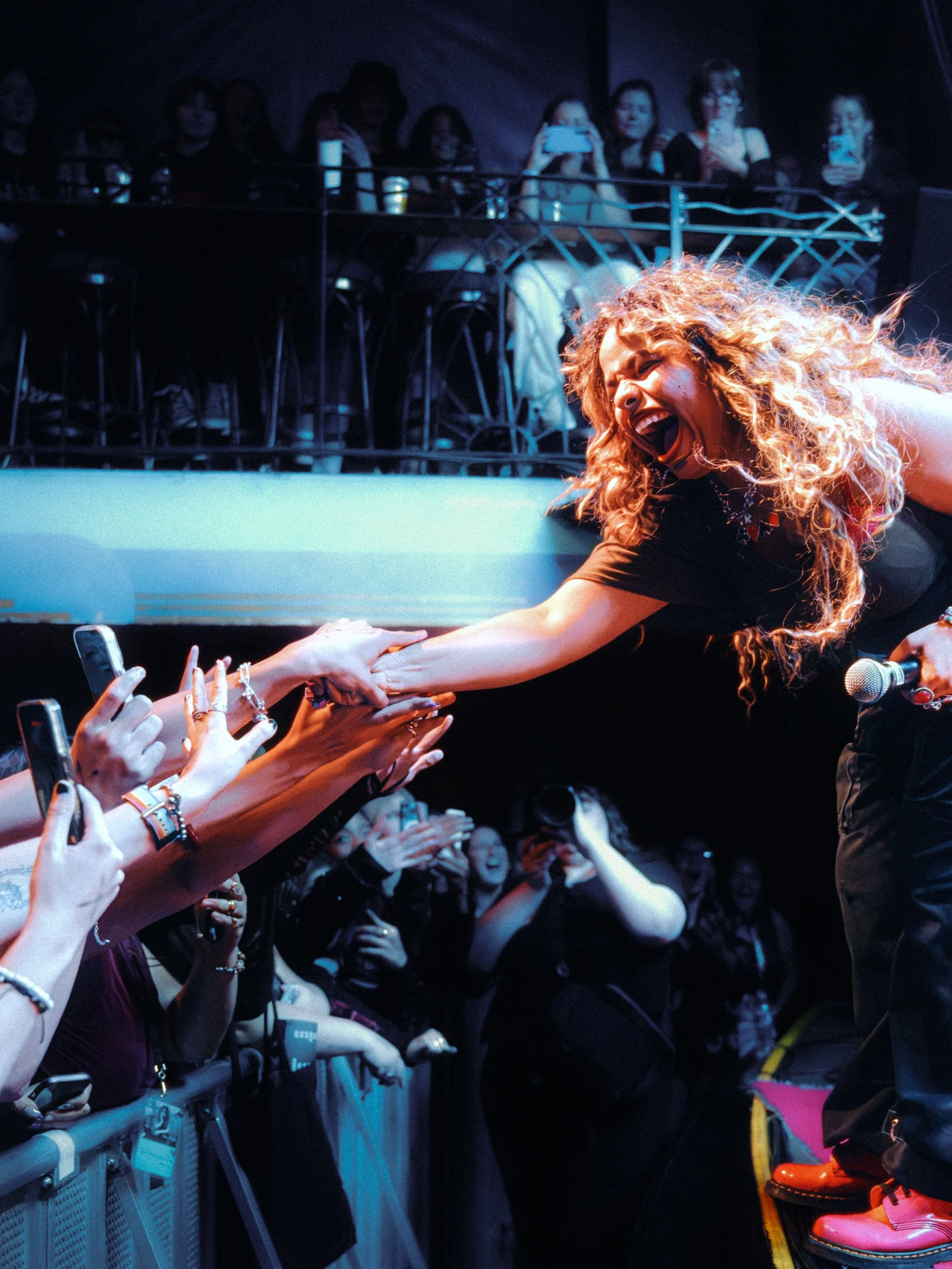 Bella Kay leaning out over the barricade into a sea of hands and phones
