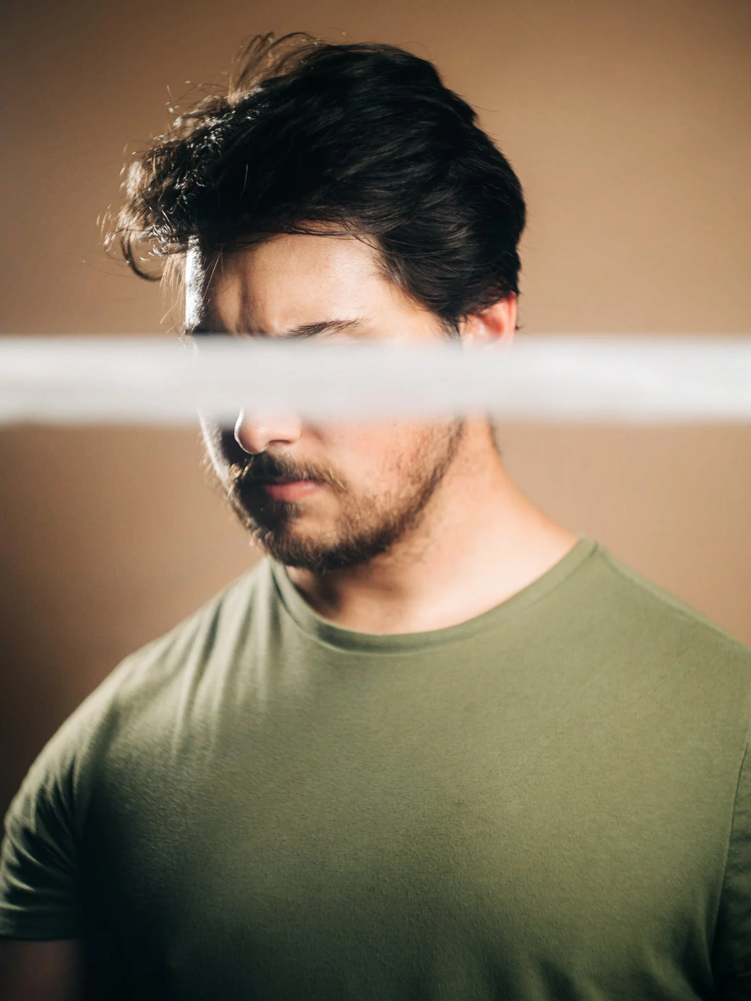 Portrait of a man with a band of light across his eyes against a tan backdrop