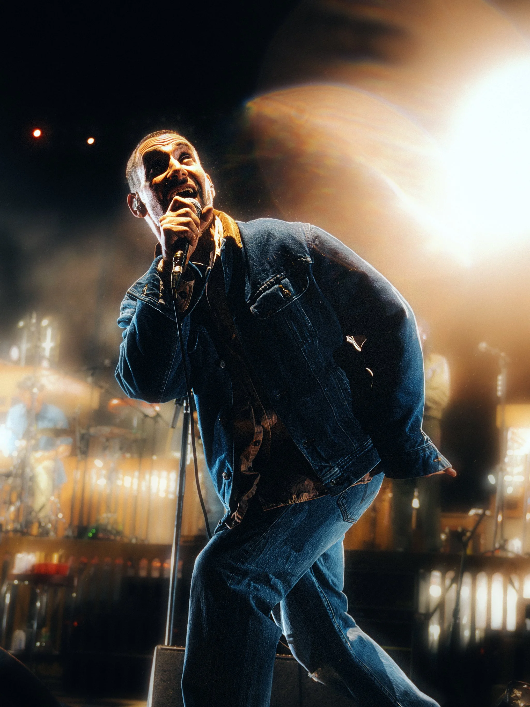 Singer in a denim jacket at the mic with a warm lens flare sweeping behind him