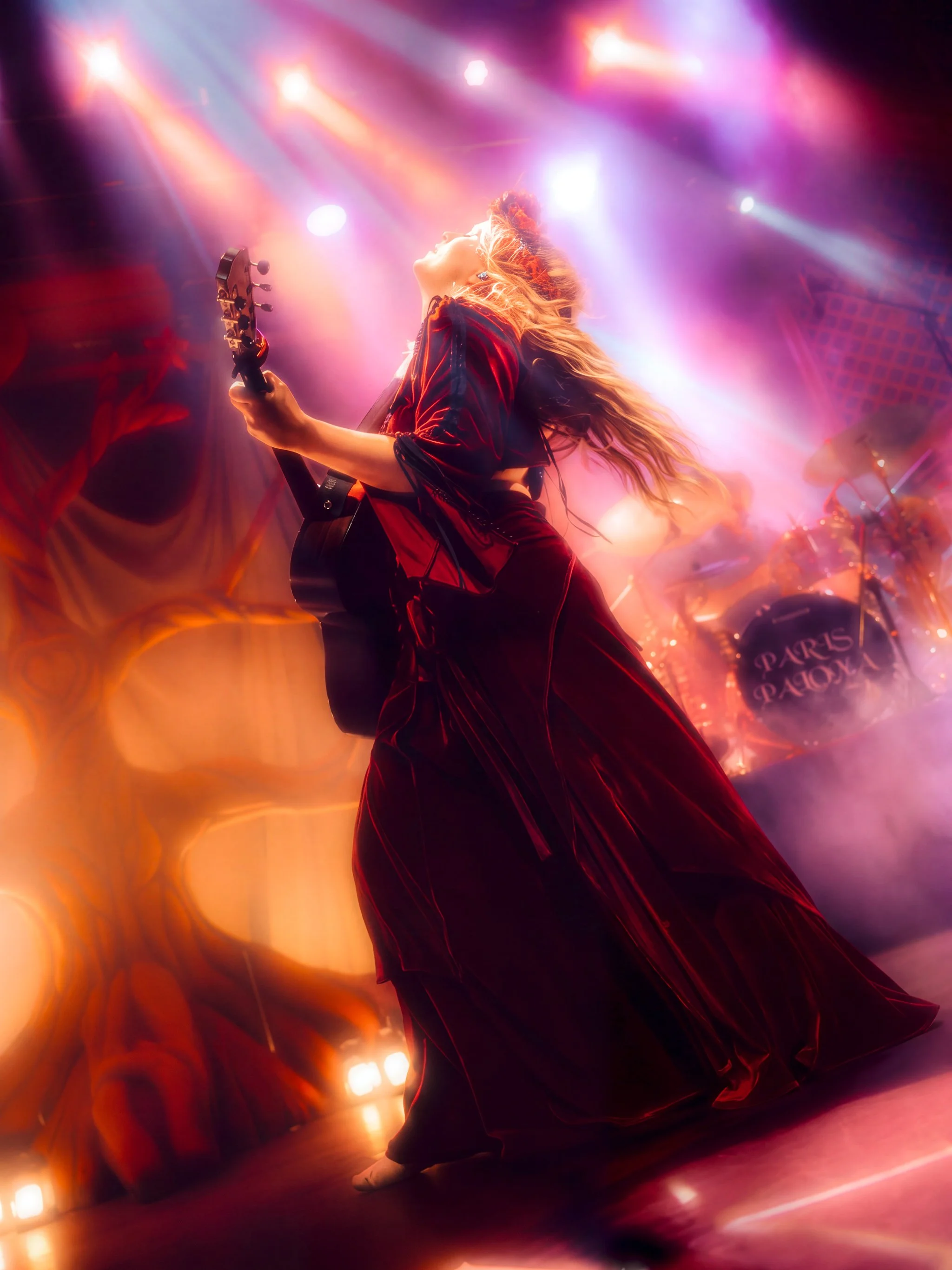 Paris Paloma with her head back under purple and orange beams, guitar in hand