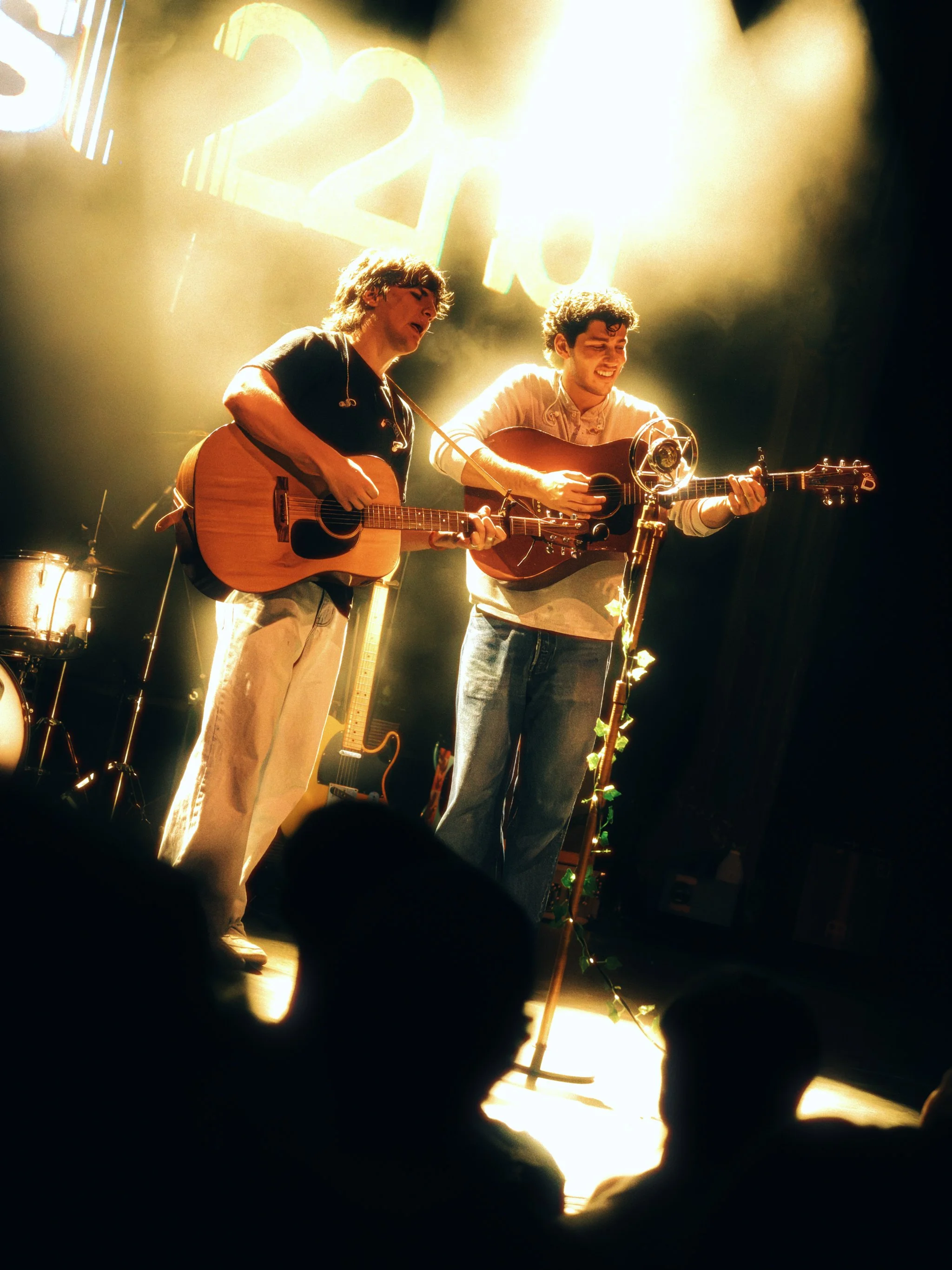Two members of West 22nd playing acoustic guitars in a warm backlight