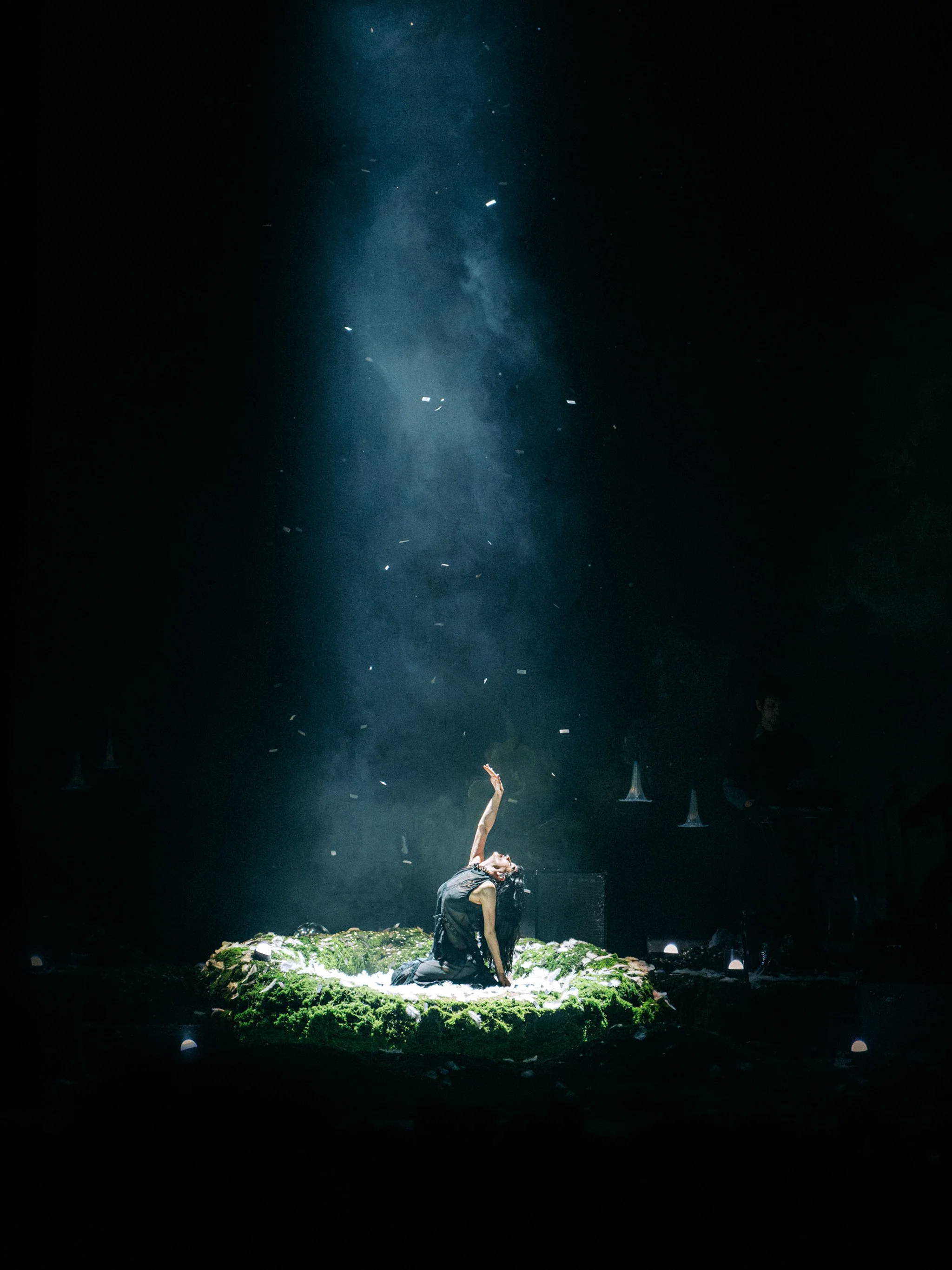 Not For Radio kneeling on a moss-covered stage under a single beam of light as paper falls through the haze. Performing at Paramount Theatre in Denver, CO
