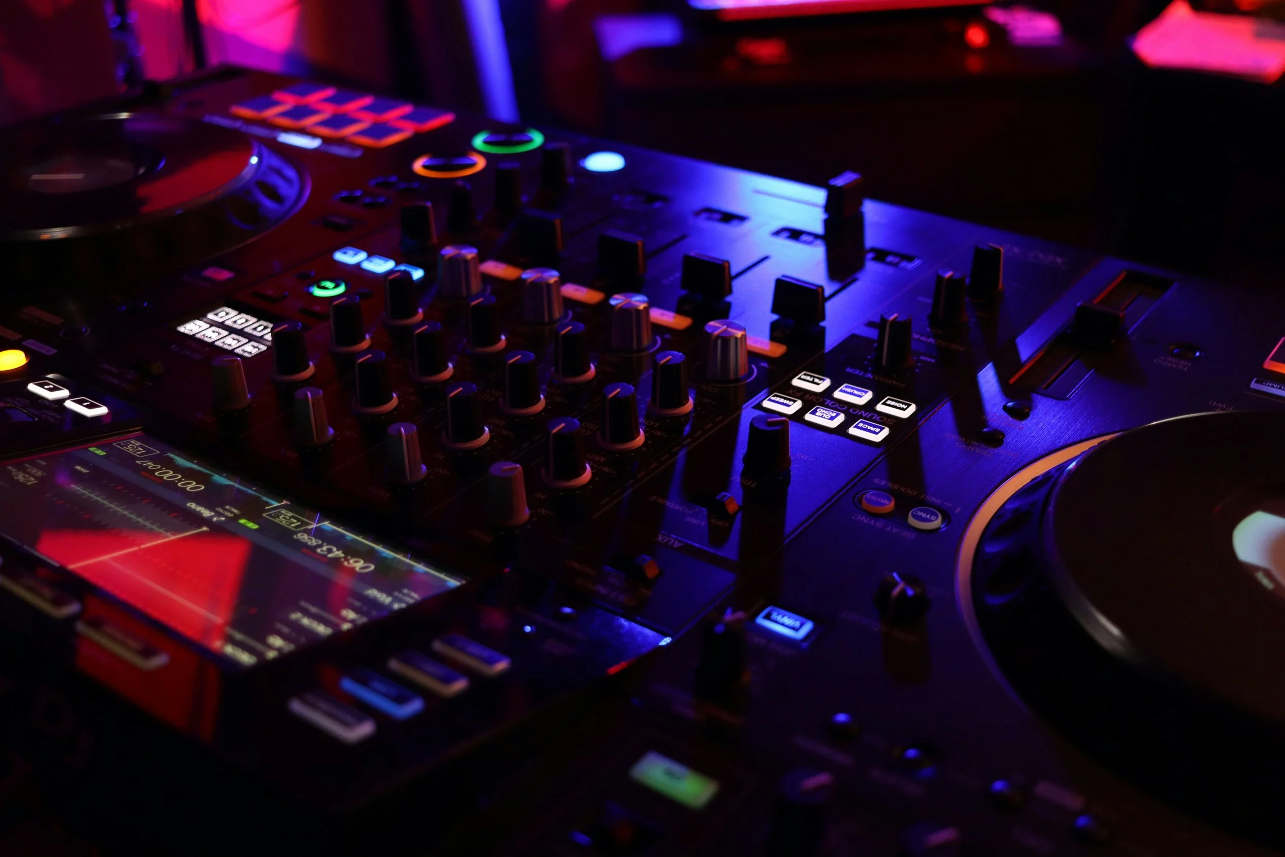 Close-up of professional DJ decks illuminated by vibrant red and blue lighting, symbolizing Passion Music’s energy, precision, and atmosphere-driven sound design for bars and lounges.