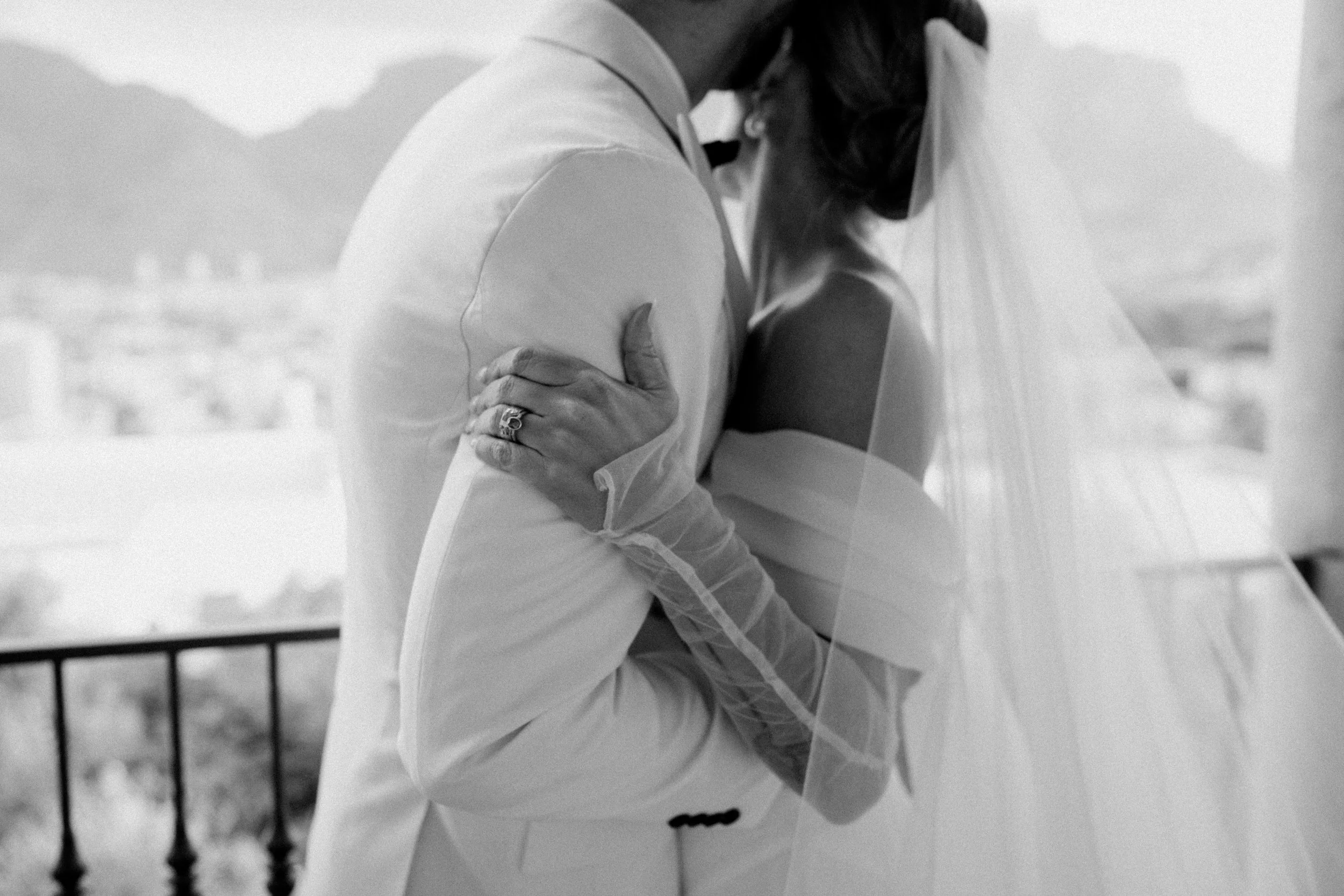 Black and white photo of a bride and groom embracing each other on a balcony.