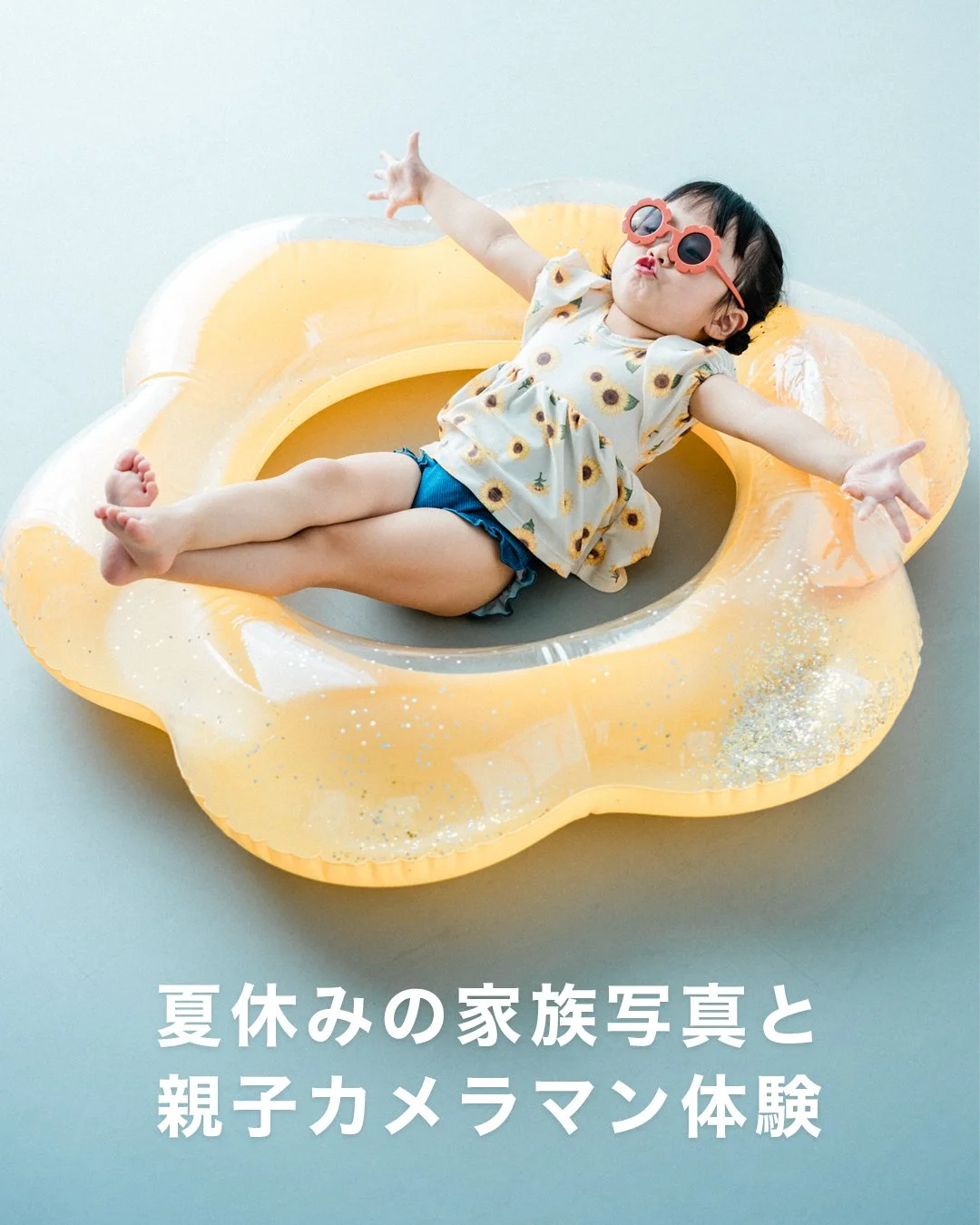 ひまわり模様の服を着た子供がサマーリングプールに寝そべっている。