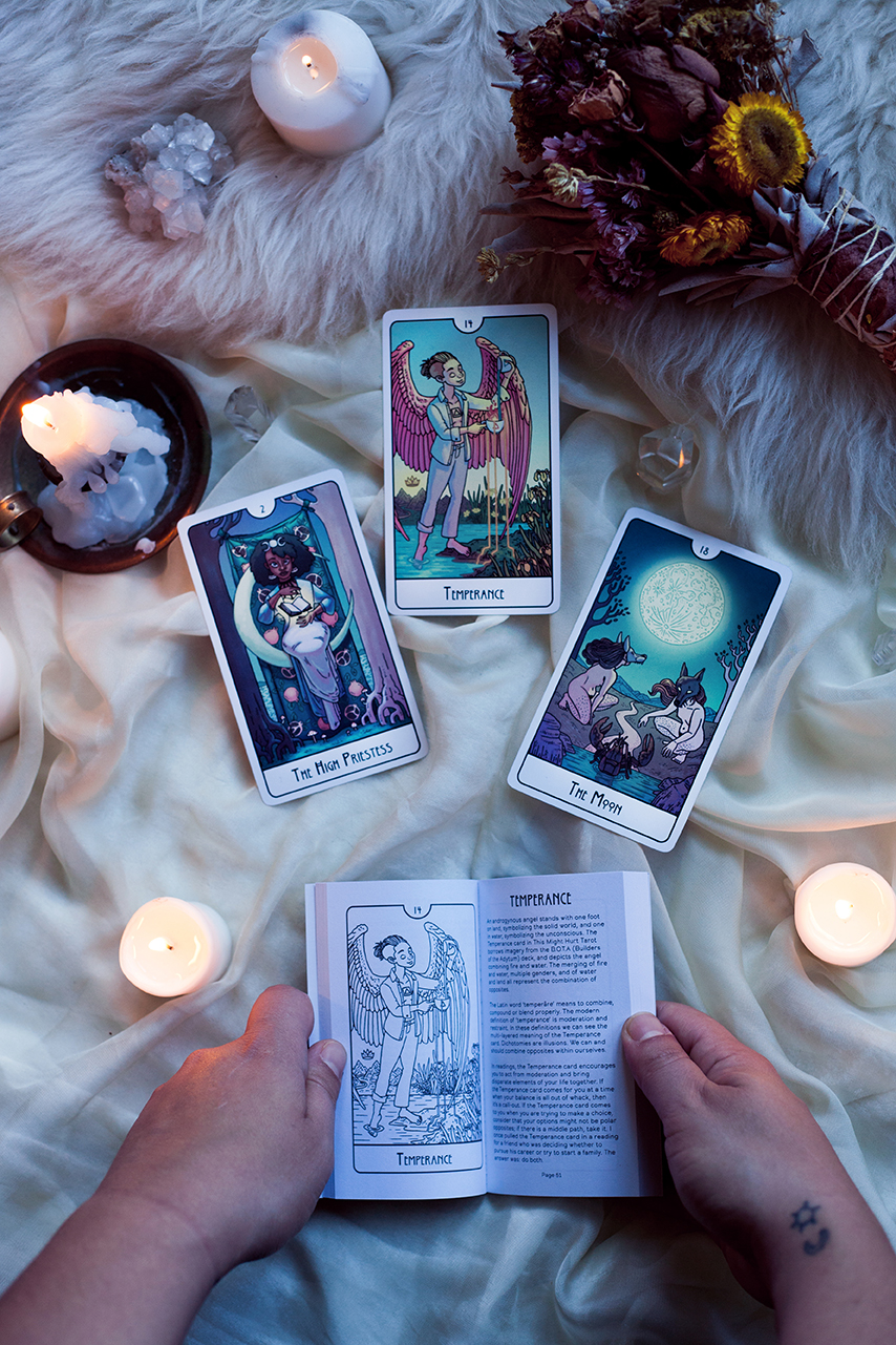  Image shows three cards surrounded by crystals and candles, with the guidebook being held open by hands beneath them. The guidebook is open to the card description for Temperance. First printing. 
