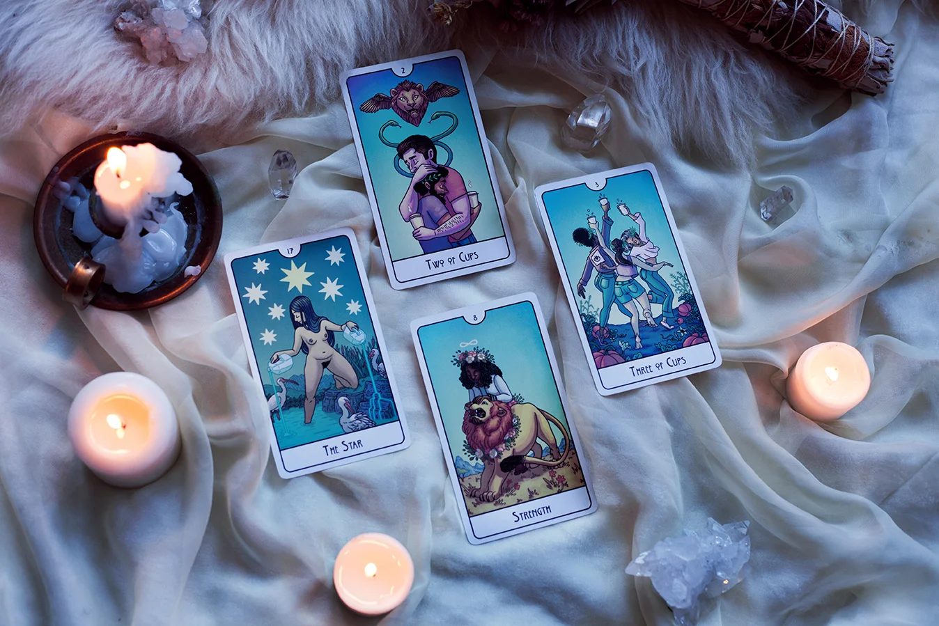 Image shows four cards surrounded by dried flowers add candles. The cards are the Star, Strength, the Two of Cups, and the Three of Cups.