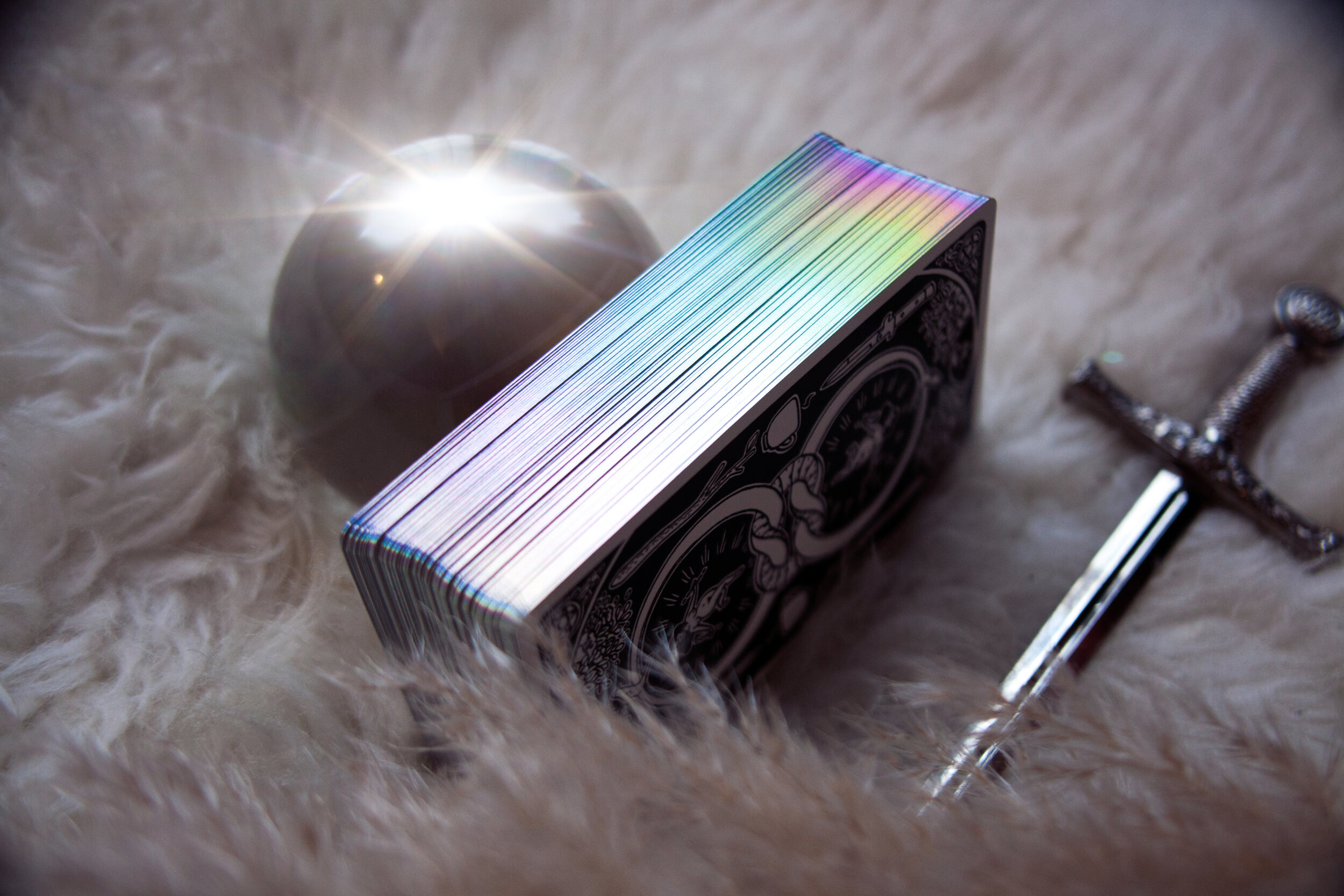  Image shows box on a white fur background. The deck has holographic pearl edges, which are silvery white with a rainbow running through them. 