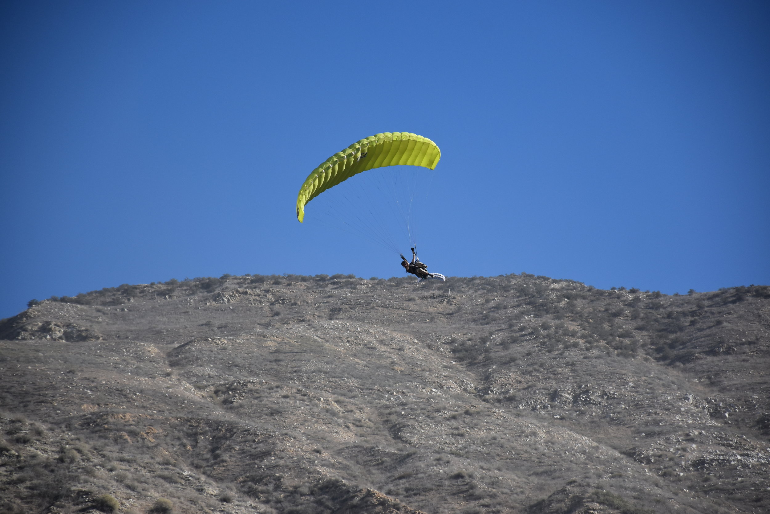 yellow paraglider landing over some hills, Soboba Flight Park, learn paragliding and paramotoring at our camp