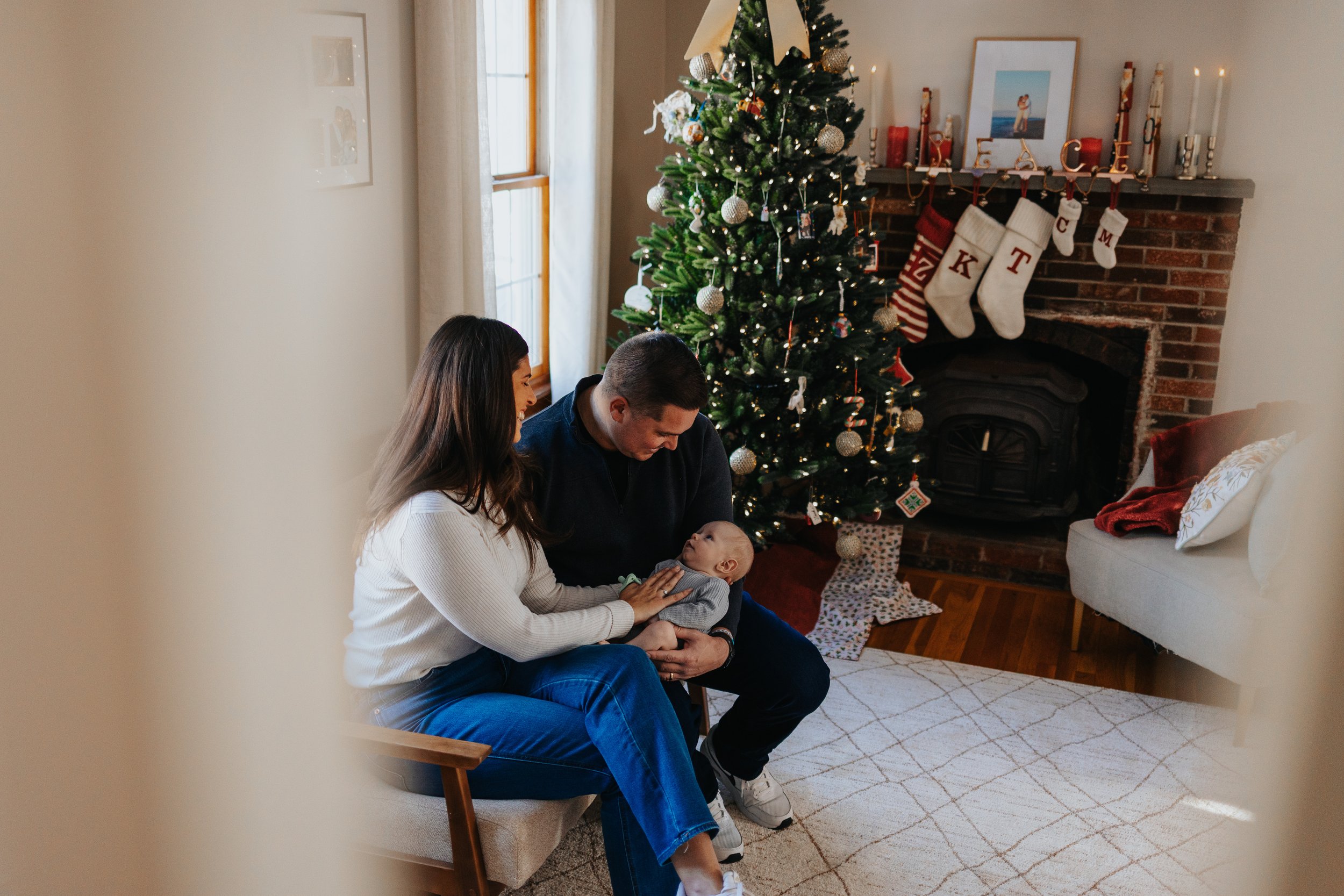 Family sitting on bench near Christmas tree during a lifestyle family portrait session in Lancaster MA.