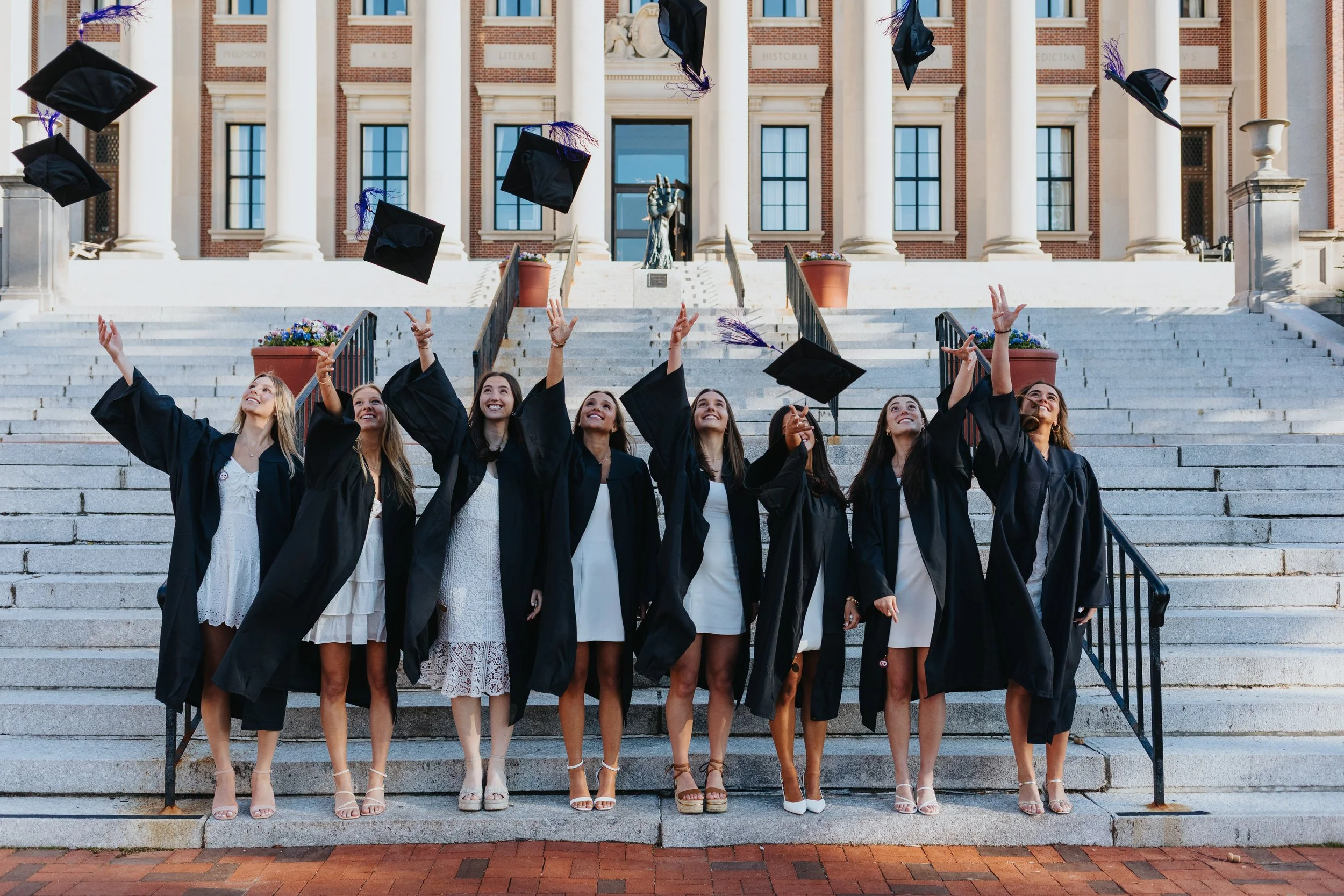 Friends throwing their caps on stairs of Dinand Library at Holy Cross during cap and gown session in Worcester.