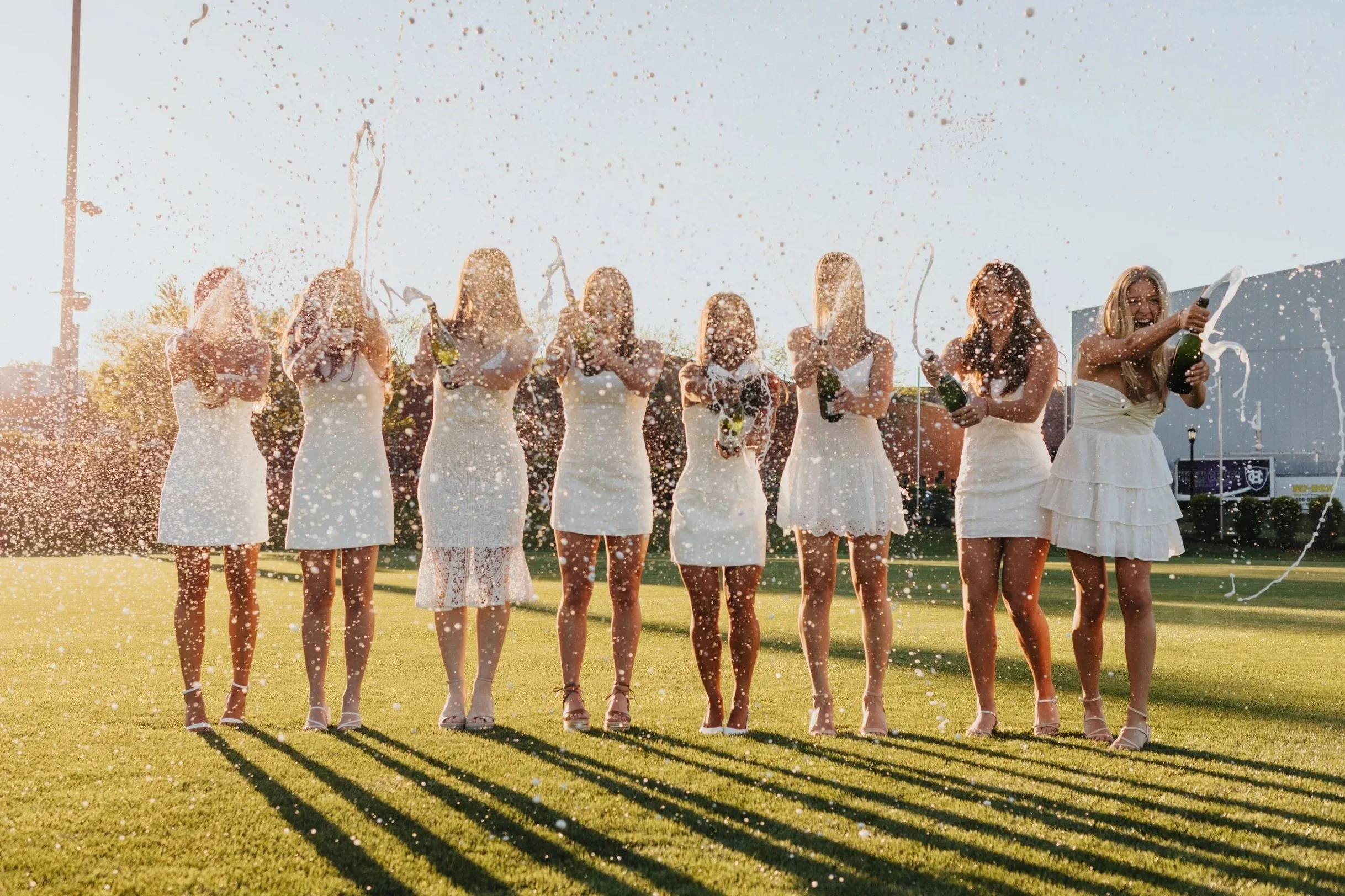 Group cap and gown photo of Holy Cross graduates spraying champagne during sunset in Worcester.