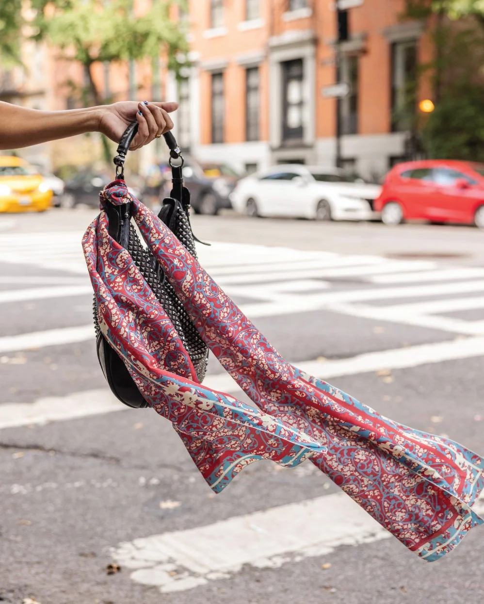 Ihsan Ishan Design Persian Patterns silk scarf with red, blue and ivory motifs styled on a handbag on a New York City street.