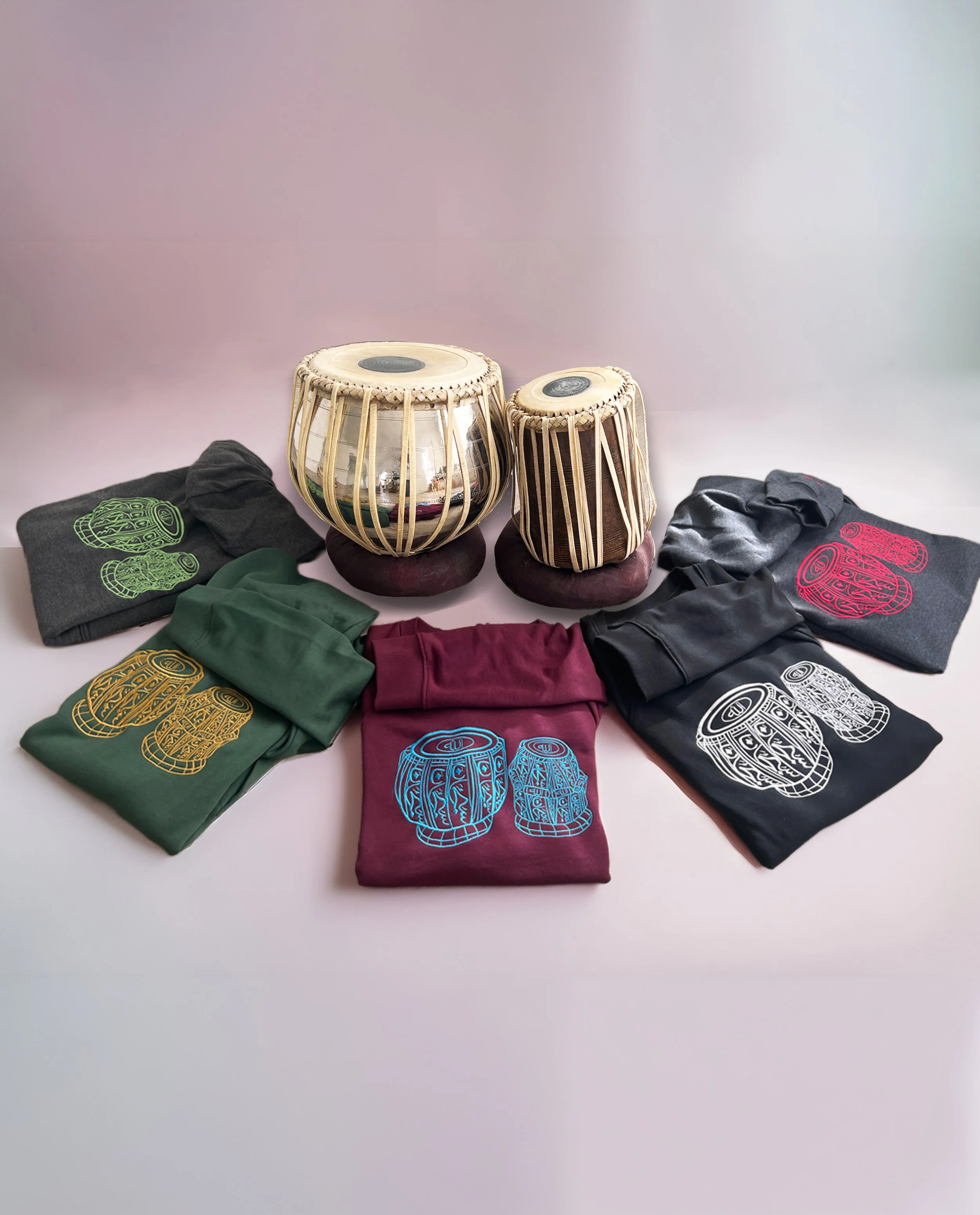 Subhanallah Tabla Collection by Ihsan Ishan Design featuring embroidered sweatshirts in multiple colors displayed with a traditional tabla set.