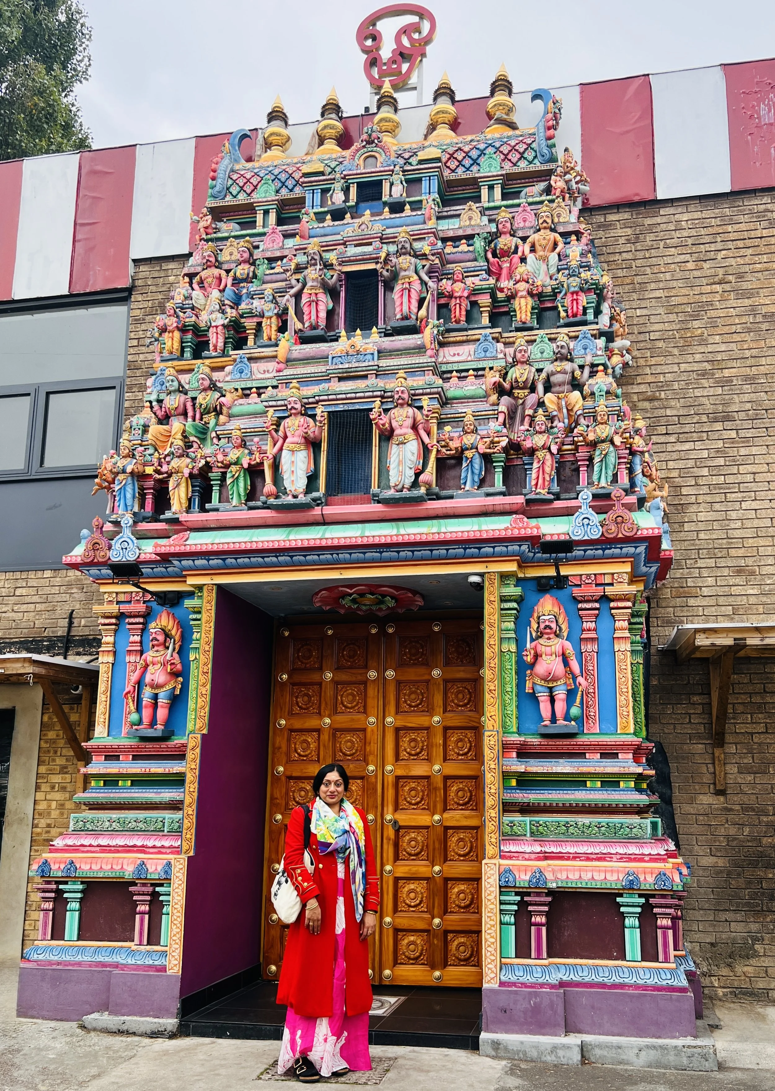 Hindu Chaplain Sangeetha Kowsik standing outside an ornate South Indian Hindu temple in London.