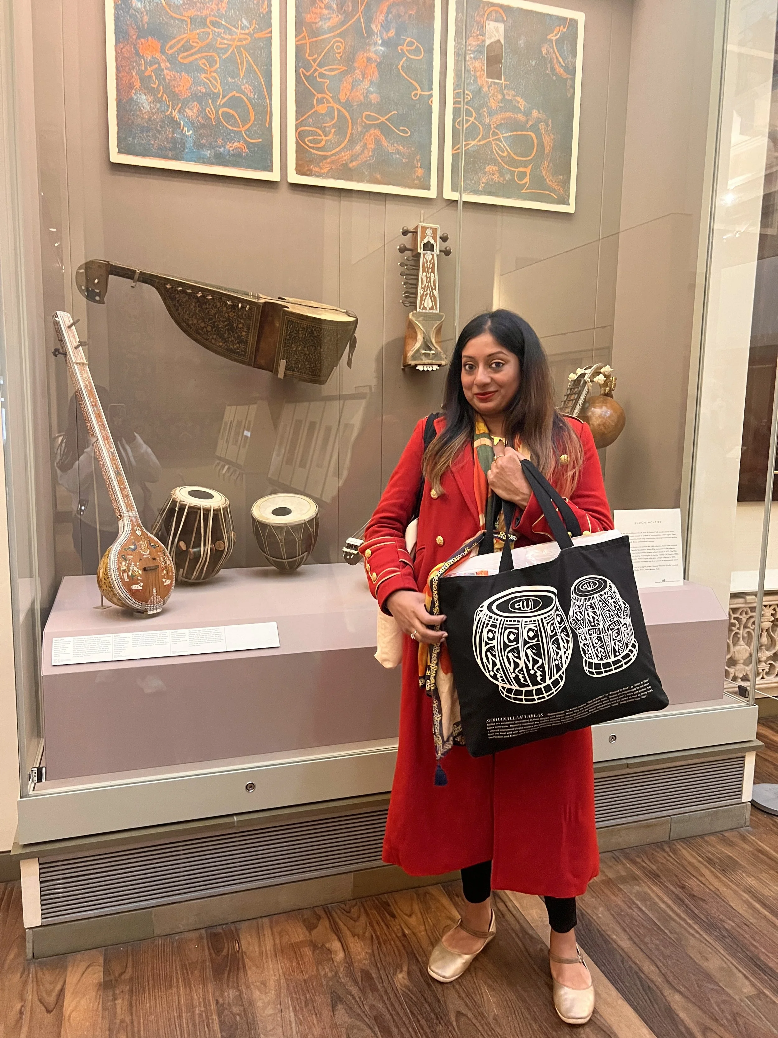 Sangeetha Kowsik, founder and creative director of Ihsan Ishan Design, carrying her Arabic calligraphy tabla bag beside a museum display of Indian musical instruments.