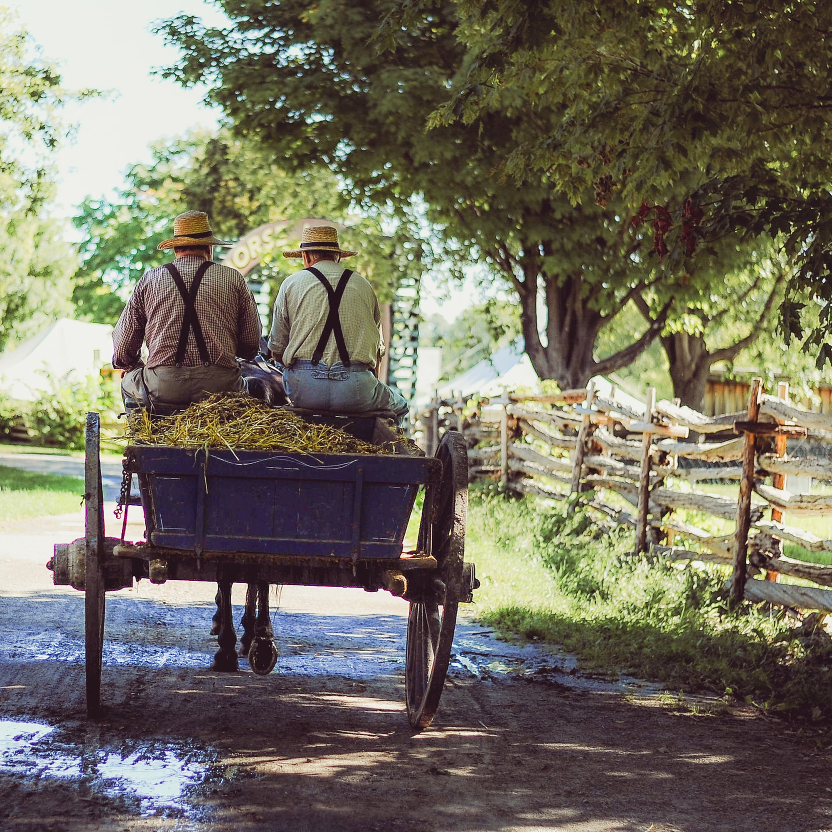 Two men ride a hay wagon down a country road.