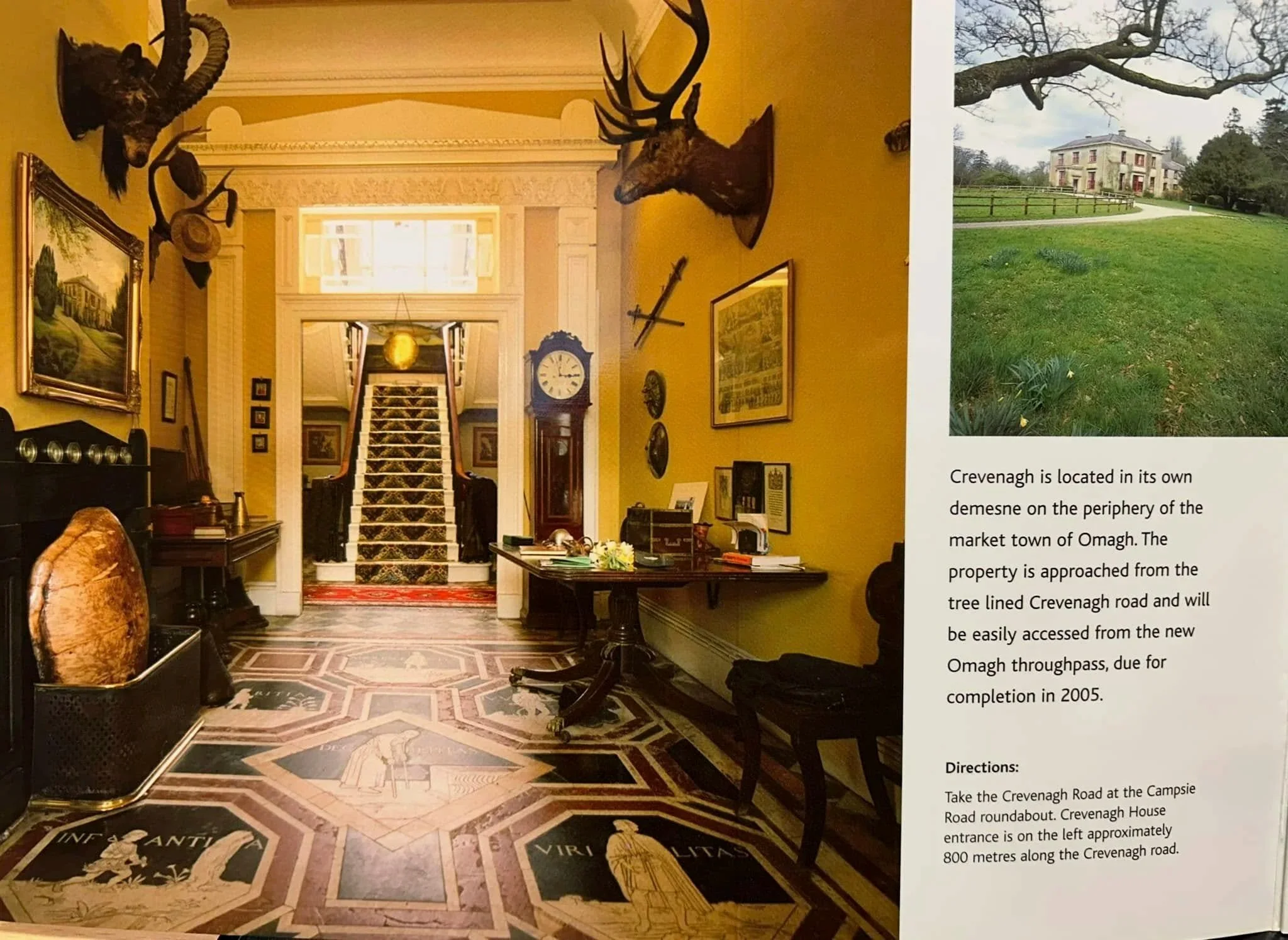 Interior of a grand house with a staircase, antique furniture, and mounted animal heads on the walls.