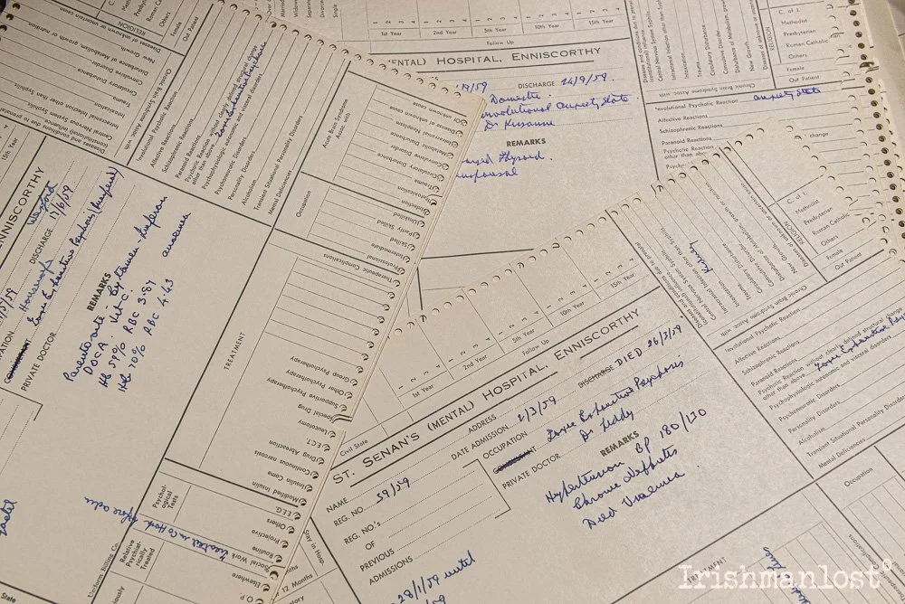 Photo of multiple handwritten and printed mental health hospital admission and discharge forms from St. Senan's Hospital, Enniscorthy, Ireland. The forms contain patient information, dates of admission and discharge, and notes.