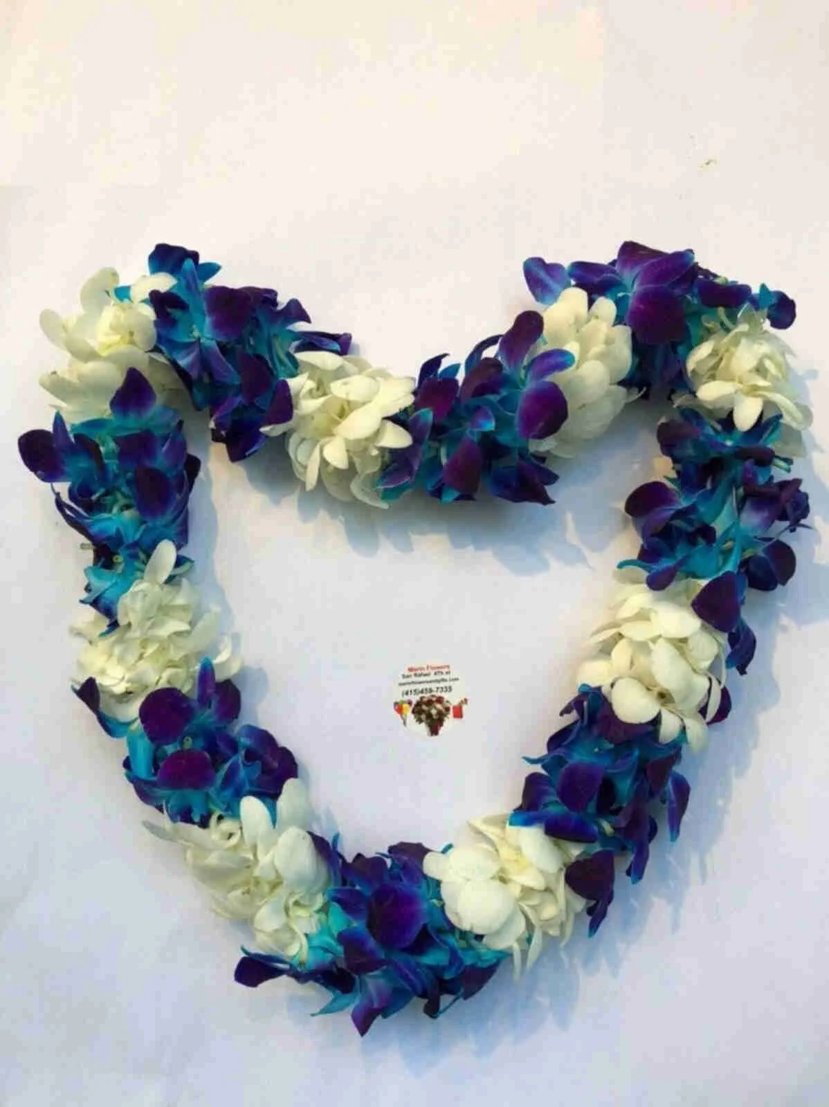A heart-shaped flower garland made of white and purple orchids hanging on a white wall.