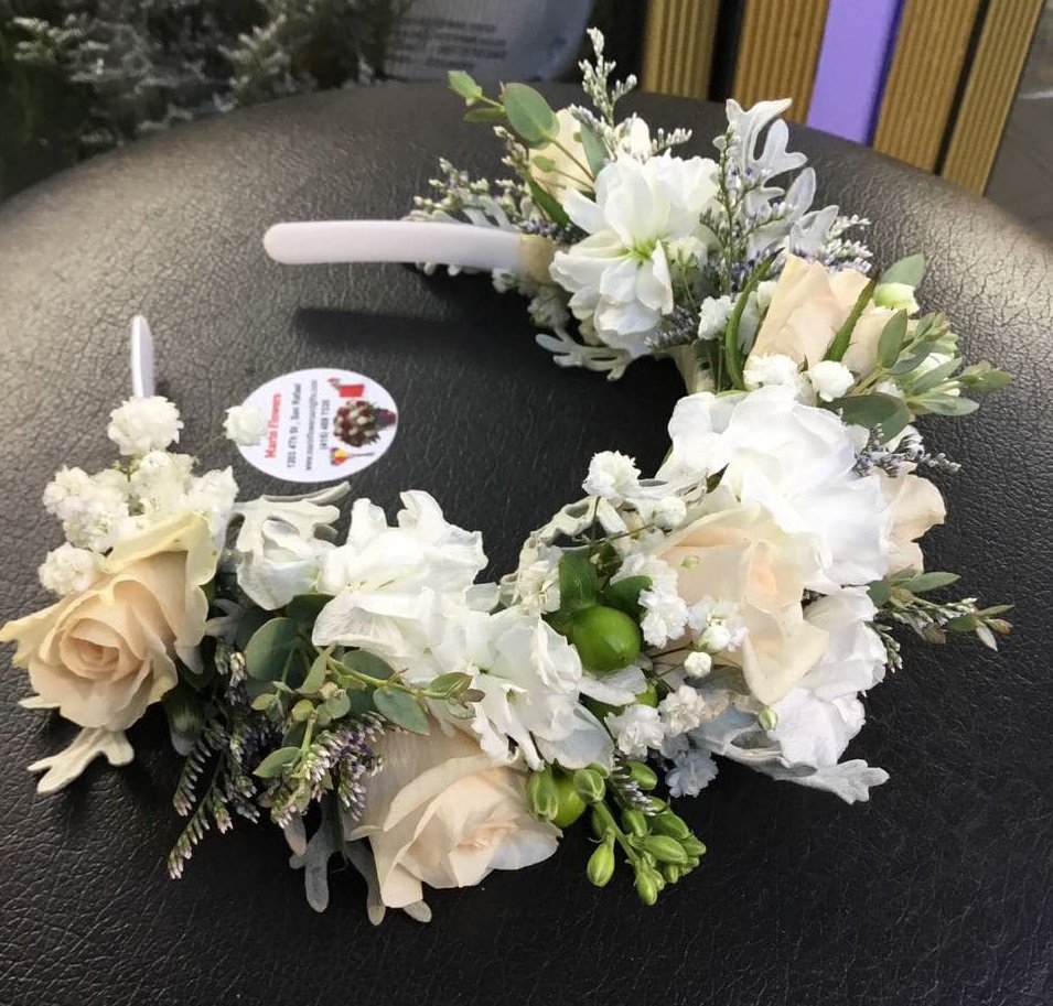 A flower crown made of white and light pink roses, white hydrangeas, and greenery, placed on a black surface.