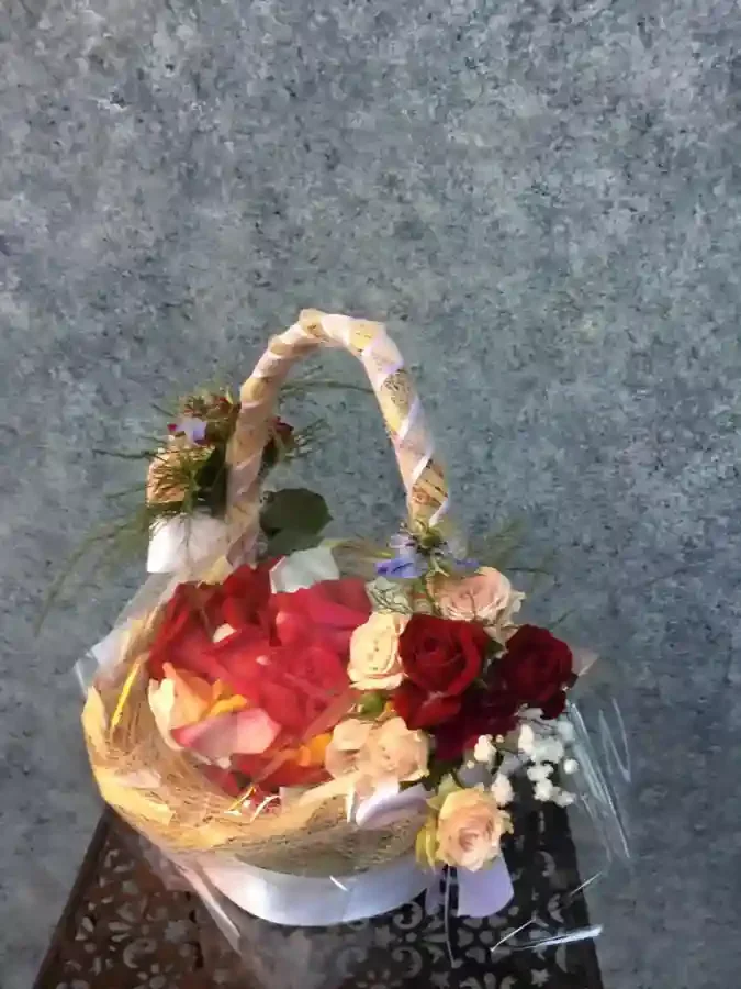 A basket filled with red roses and other assorted flowers on a gray surface.