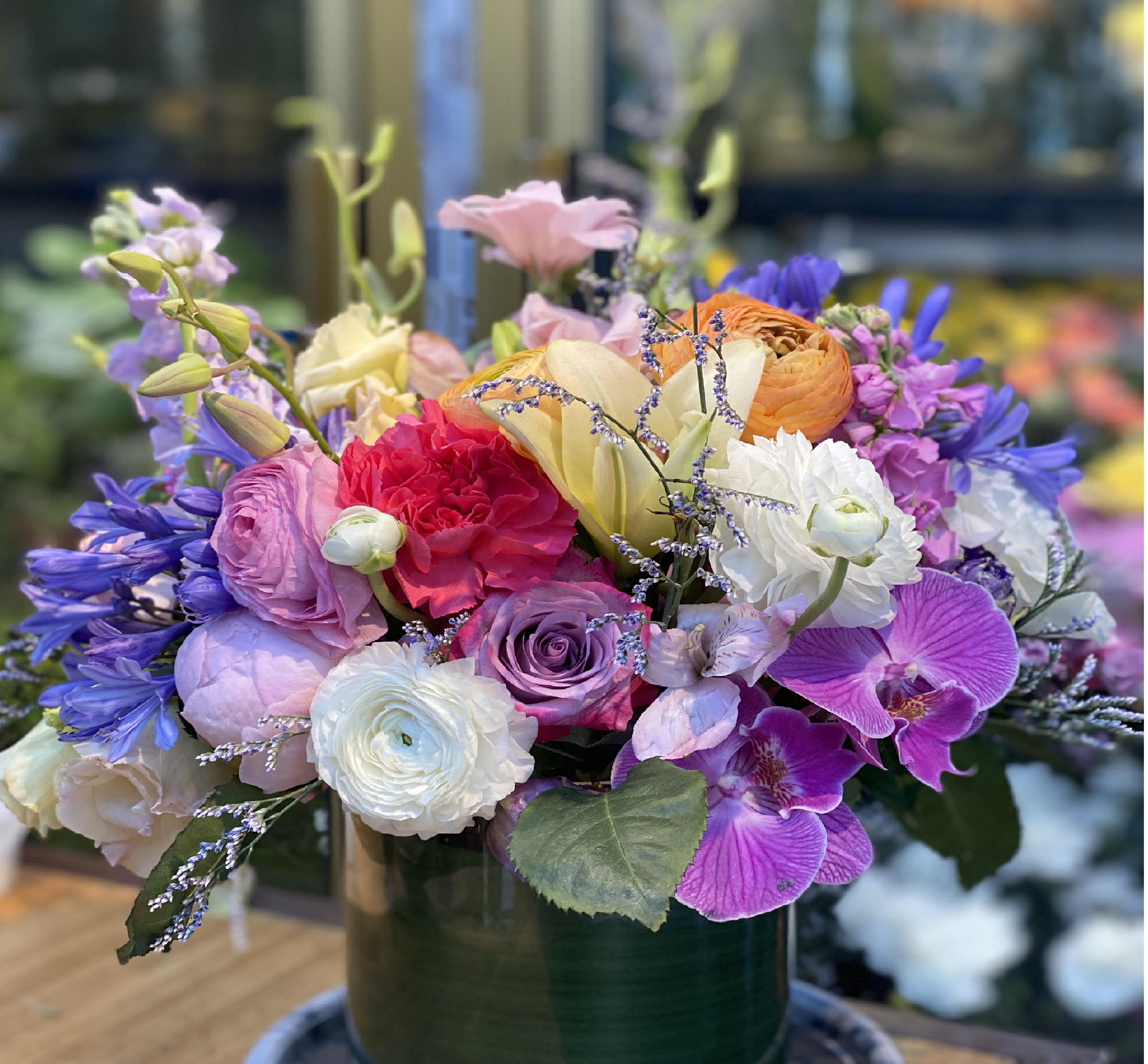 A colorful bouquet of various flowers including roses, orchids, lisianthus, and other blooms in a dark green vase.