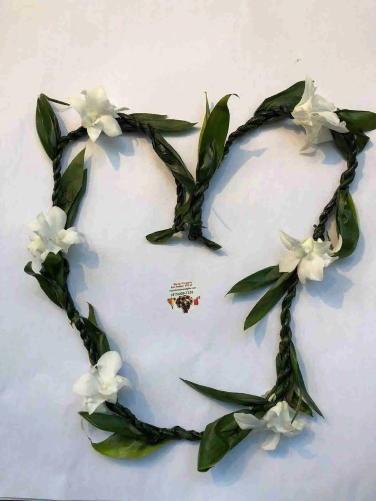 Heart-shaped floral arrangement made of twisted green leaves and white flowers on white background, with a small business card underneath.