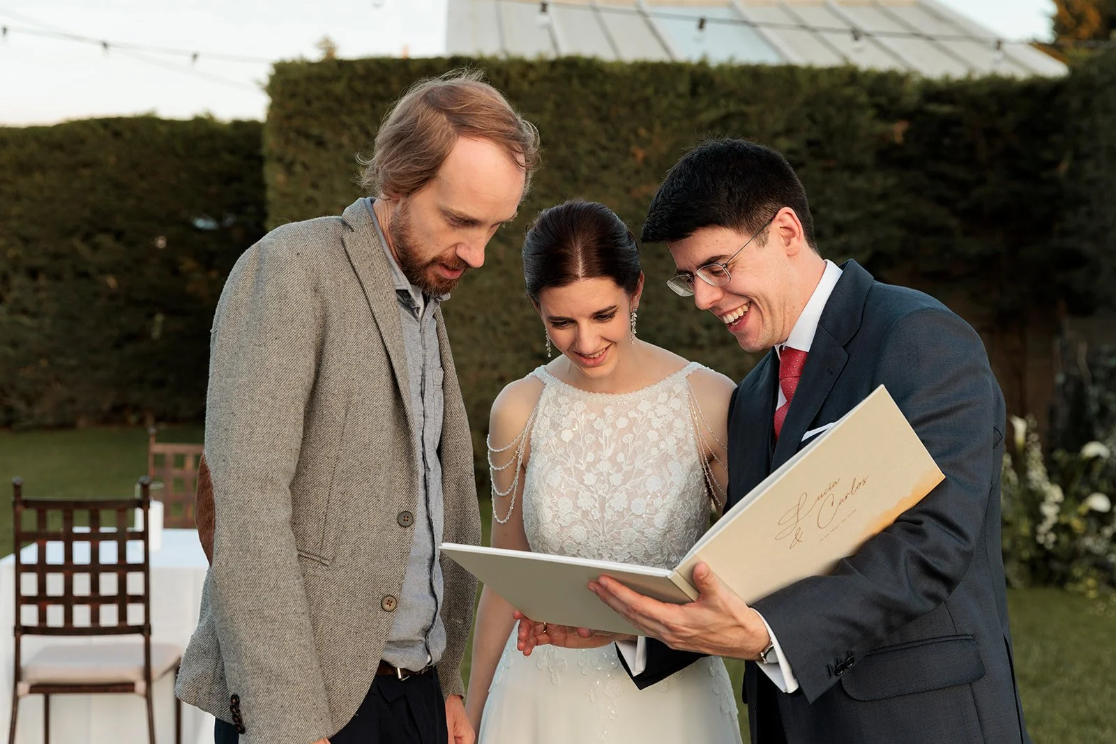Una pareja de novios en su boda con artista Nathan Brenville, mirando su álbum ilustrado en un jardín al atardecer.