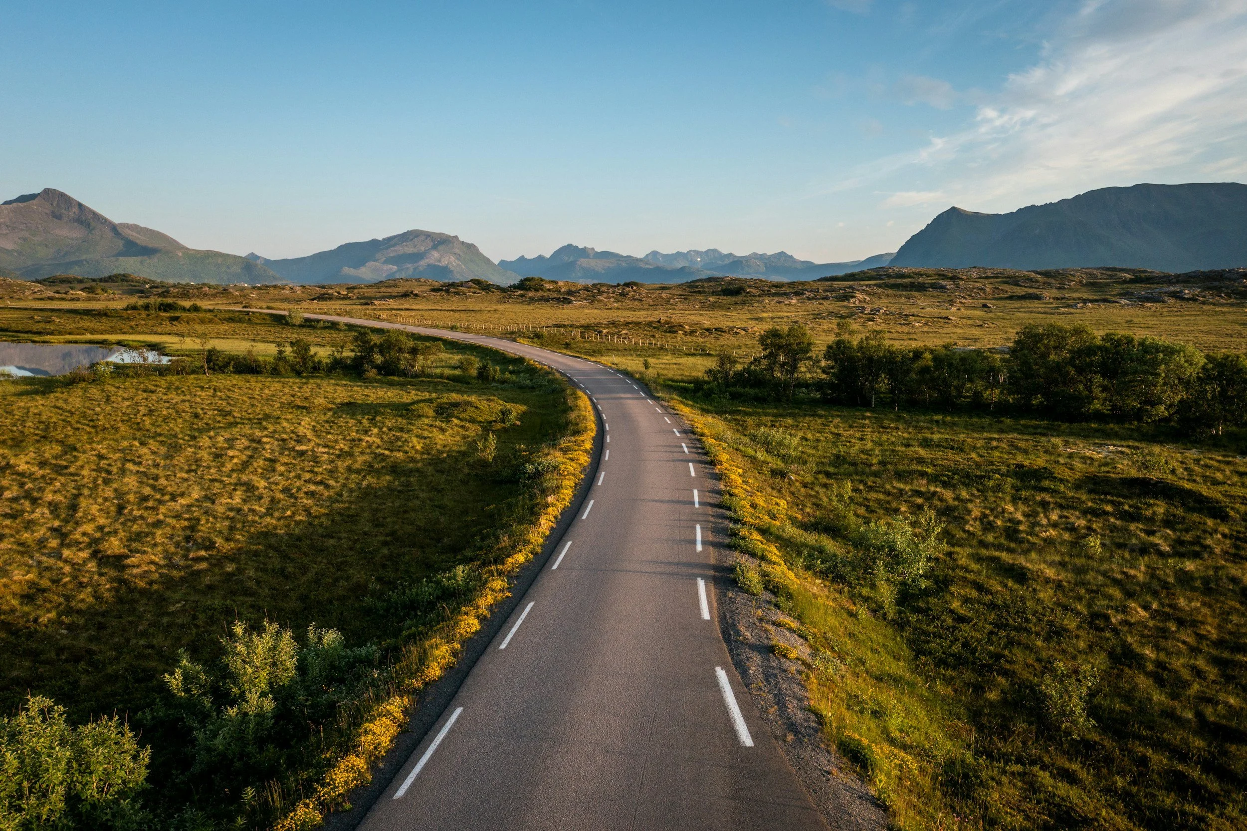 A two-lane road stretches into the distance through open countryside, winding toward mountains on the horizon.