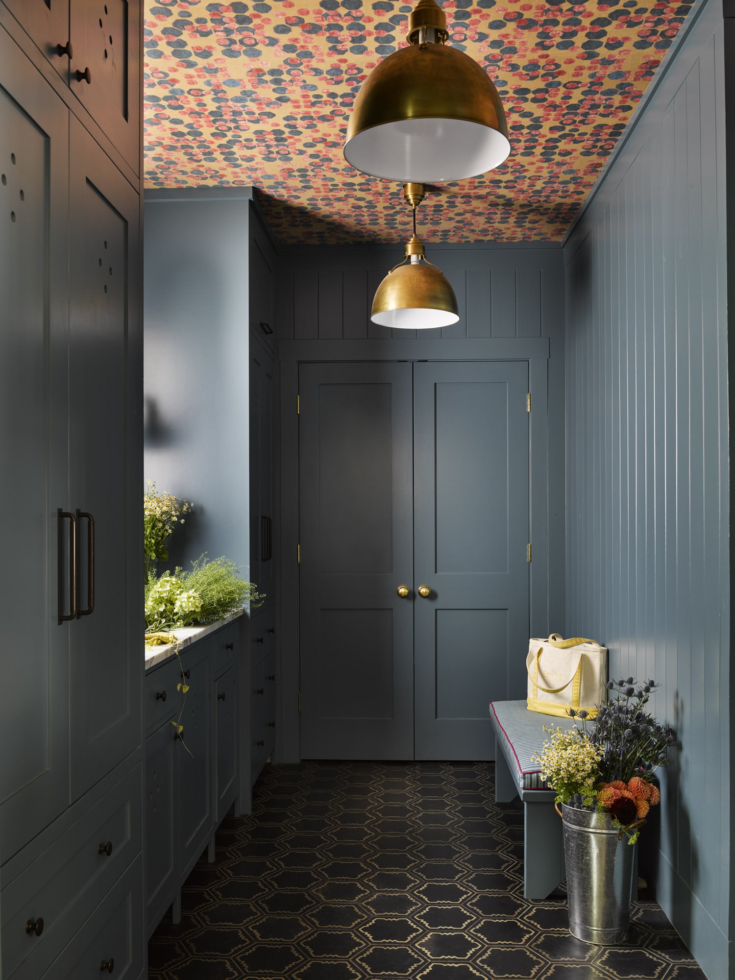  THE MUDROOM FEATURES PATTERNED CEMENT TILES FROM MOSAIC HOUSE, CABINETS PAINTED BENJAMIN MOORE BELLA BLUE 720, BURNISHED BRASS PENDANT LIGHTS FROM VISUAL COMFORT, AND WALLPAPER ON THE CEILING FROM LEE JOFA.  