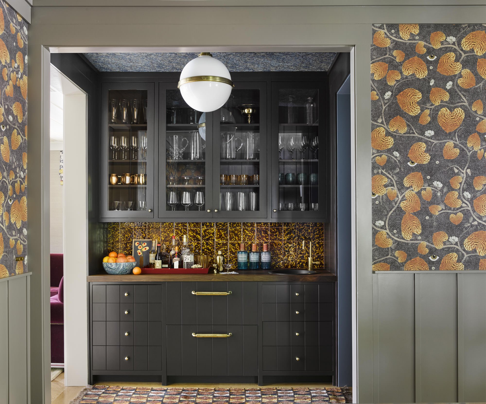   IN THE BAR, CABINETRY CONCEALING THE FRIDGE DRAWERS IS PAINTED FARROW &amp; BALL TANNER’S BROWN NO. 255. A VINTAGE RUNNER FROM RUG &amp; KILIM, TORTOISE CERAMIC TILE BACKSPLASH FROM BALINEUM, A PENDANT LIGHT FROM VISUAL COMFORT, MARBLEIZED WALLPAPE