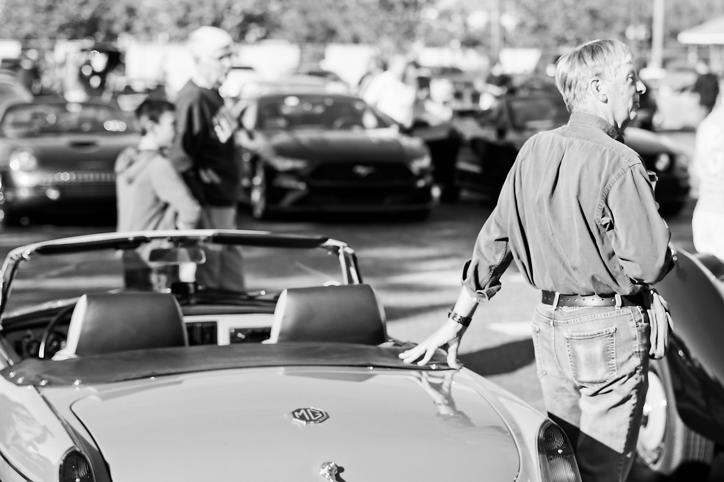  black and white image of a man placing his hand on a vintage MG at a car show 