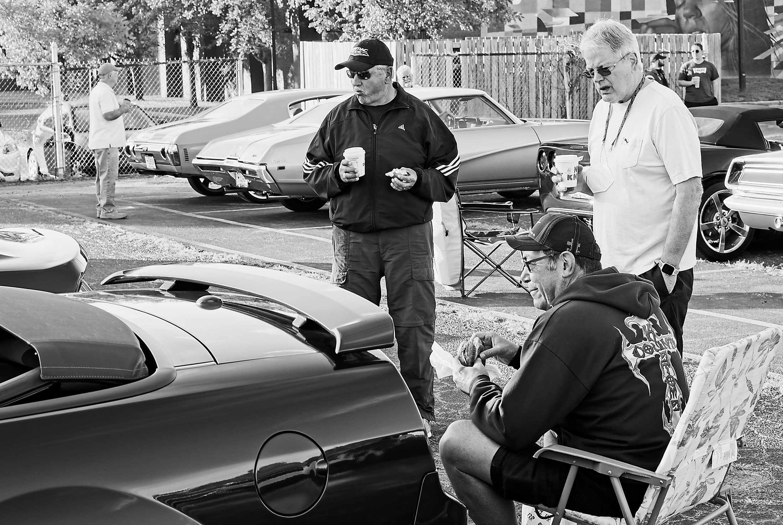  black and white image of three man looking at a car at a vintage car show, one is seated 