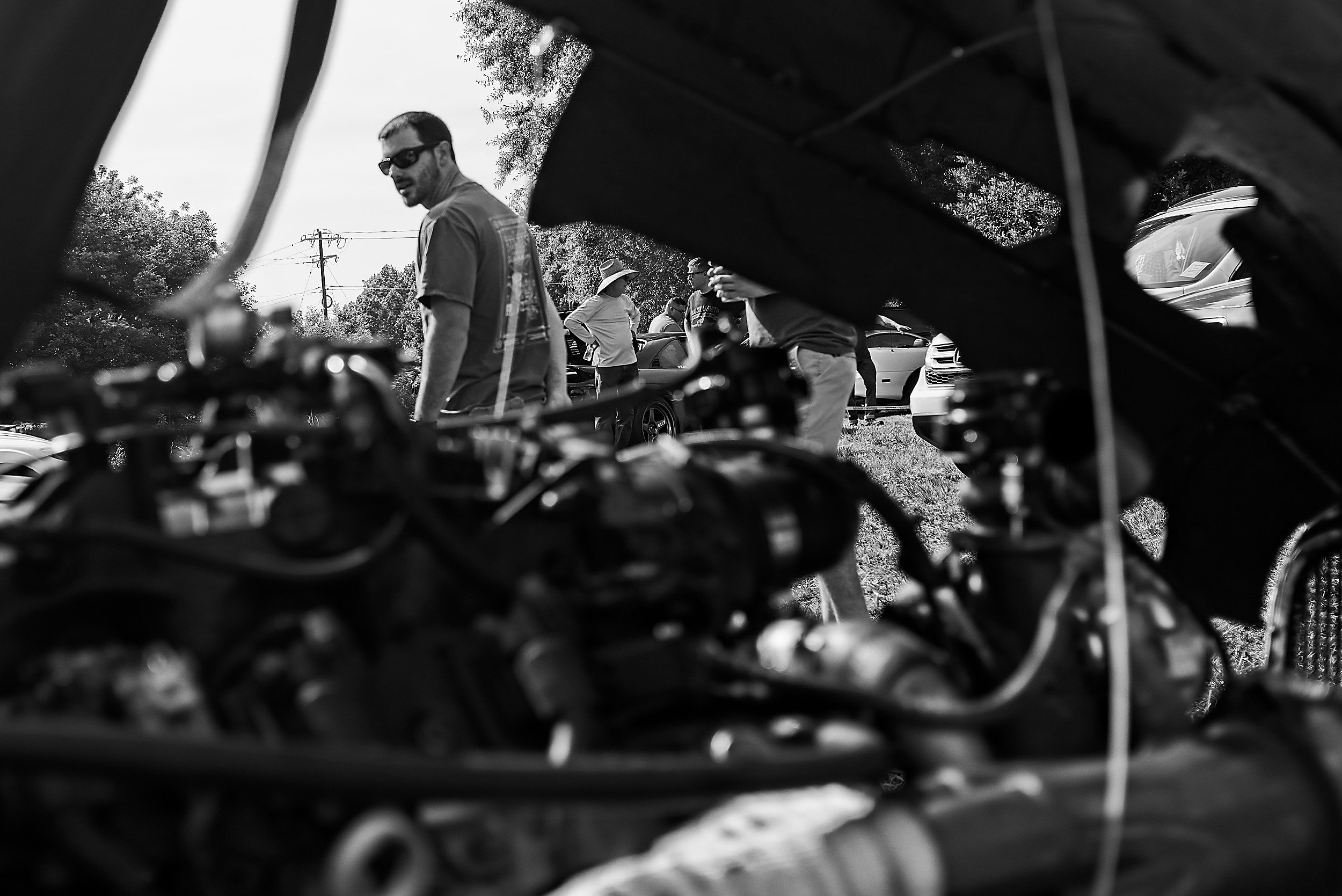  black and white image of a man with sunglases looking at the engine of a vintage car 