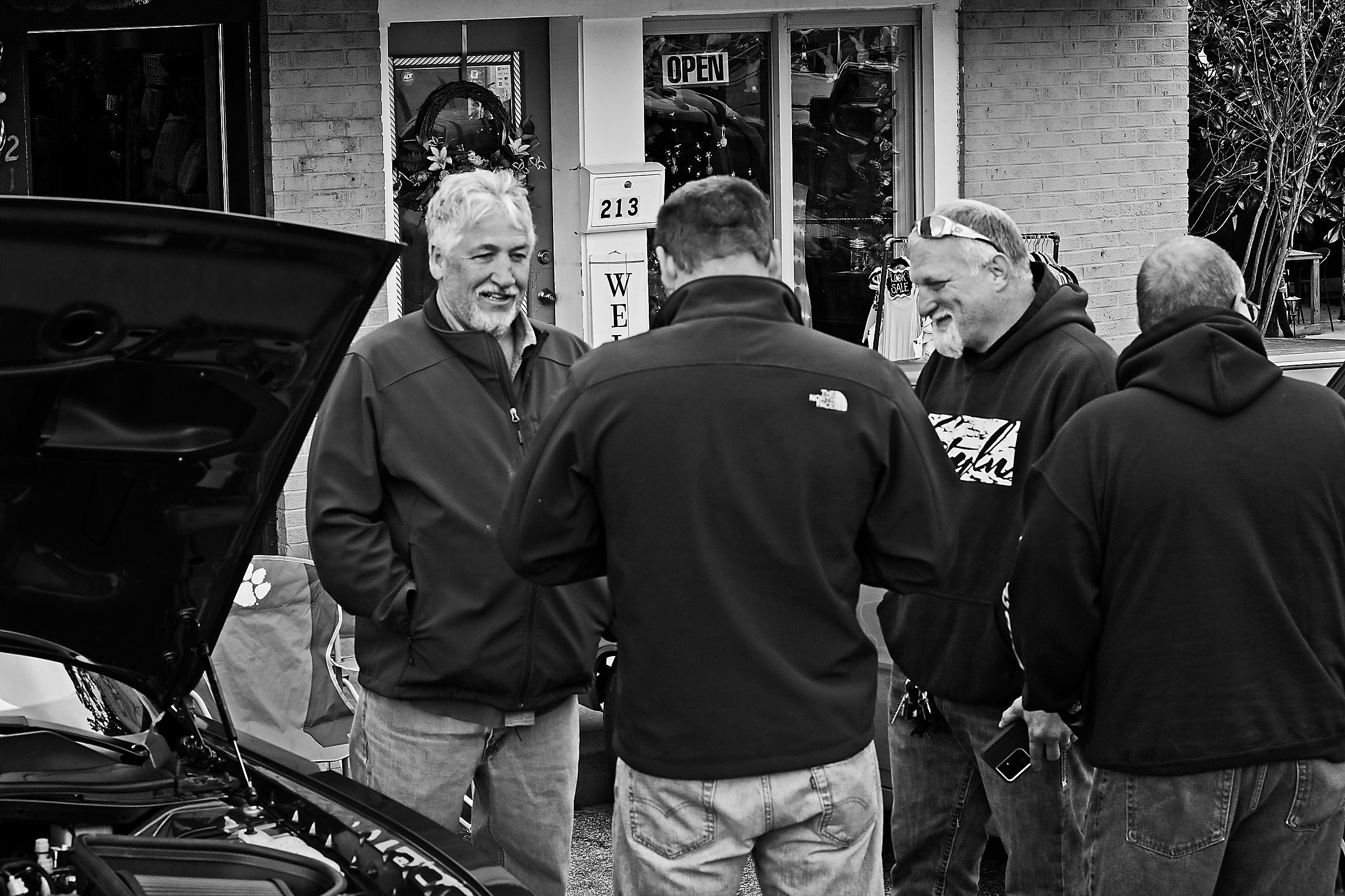  black and white image of four men talking at a car show 