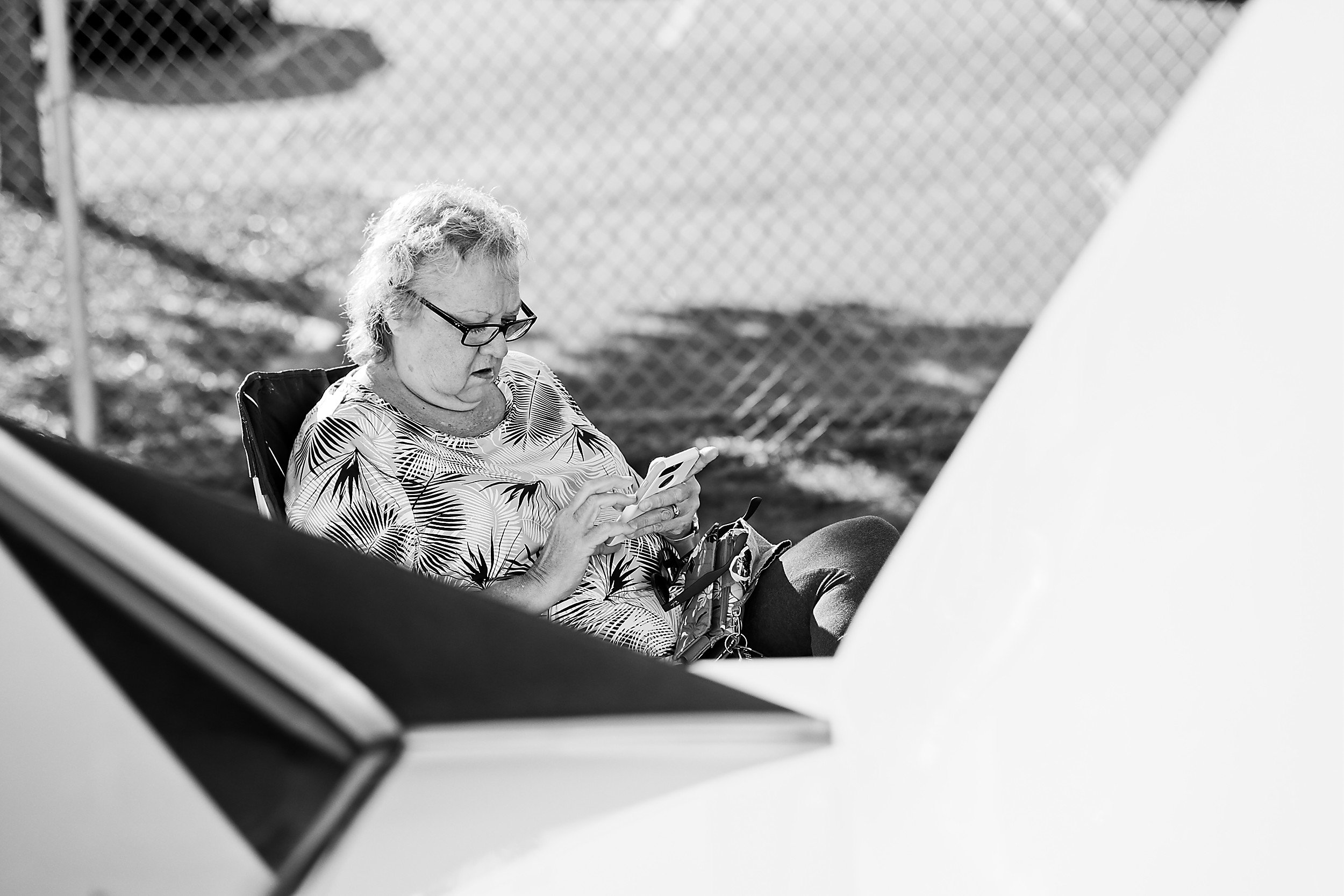  black and white image of a sitting woman reading at a car show 