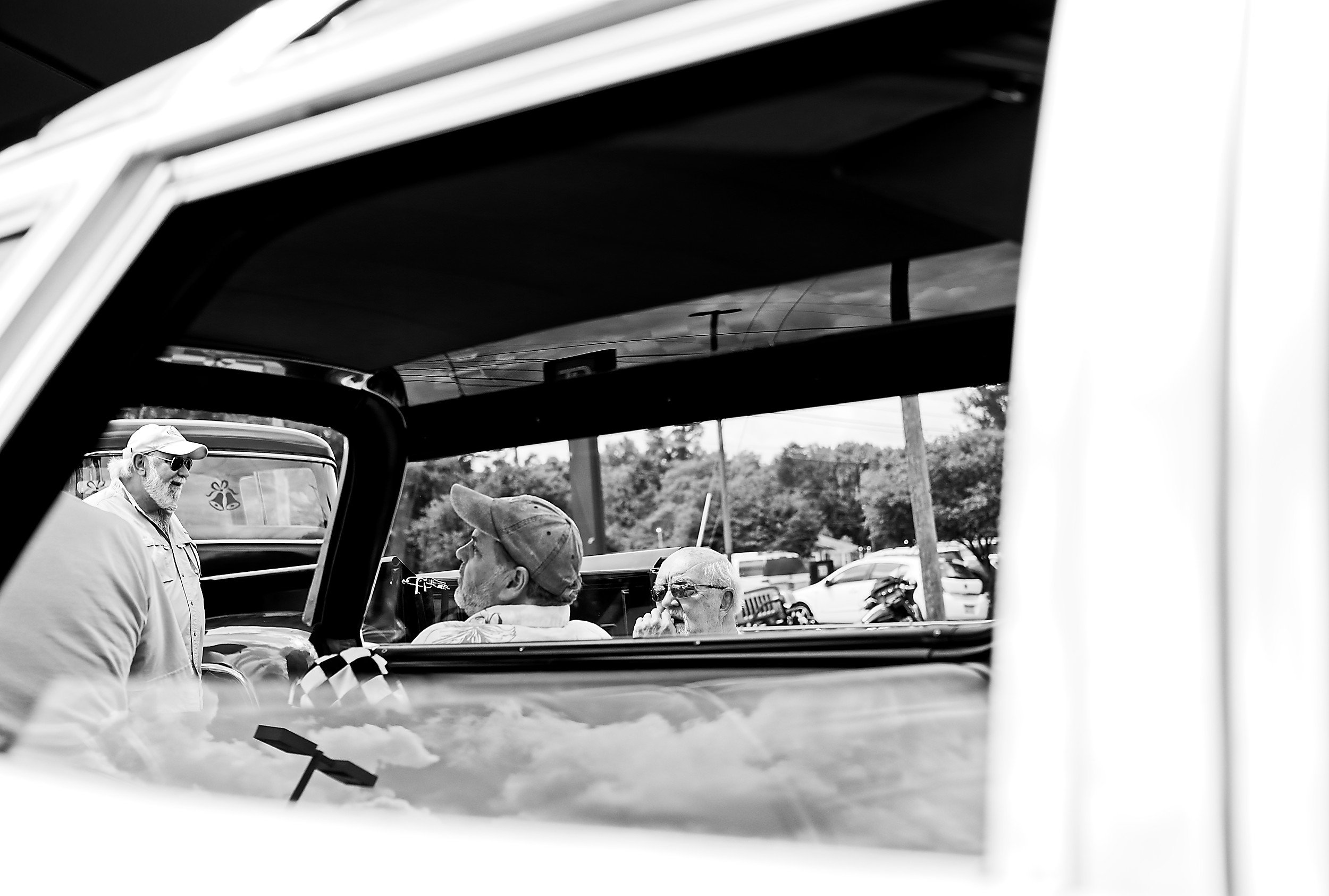  black and white image of several men as seen through the windows of a car 