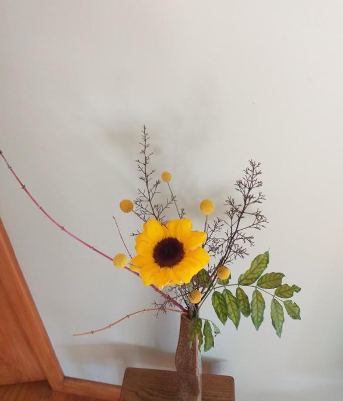 Highlighting a sunflower in Sandi's arrangement for a low coffee table. IMaterial include craspedia- Billy buttons, wisteria leaves, nandina and maple.
