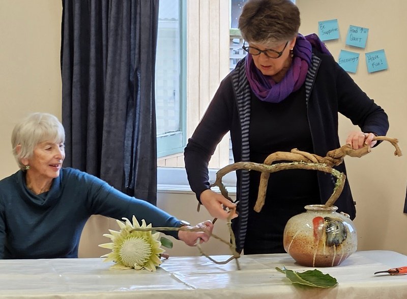 Sandi helping Alyson balance a large branch across a beautiful pottery vase
