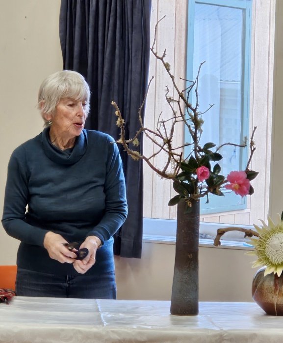 Sandi explaining her arrangement of lichen covered branches with camellia in a tall pottery vase