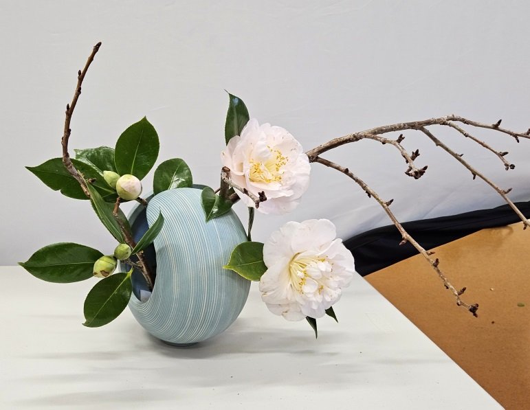 In a beautiful container, Elizabeth arranged bare branches with camellia flowers and leaves