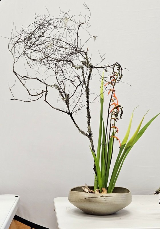 In a low pottery container, Nicole arranged bare branches with tall orange flowers and budding lilies