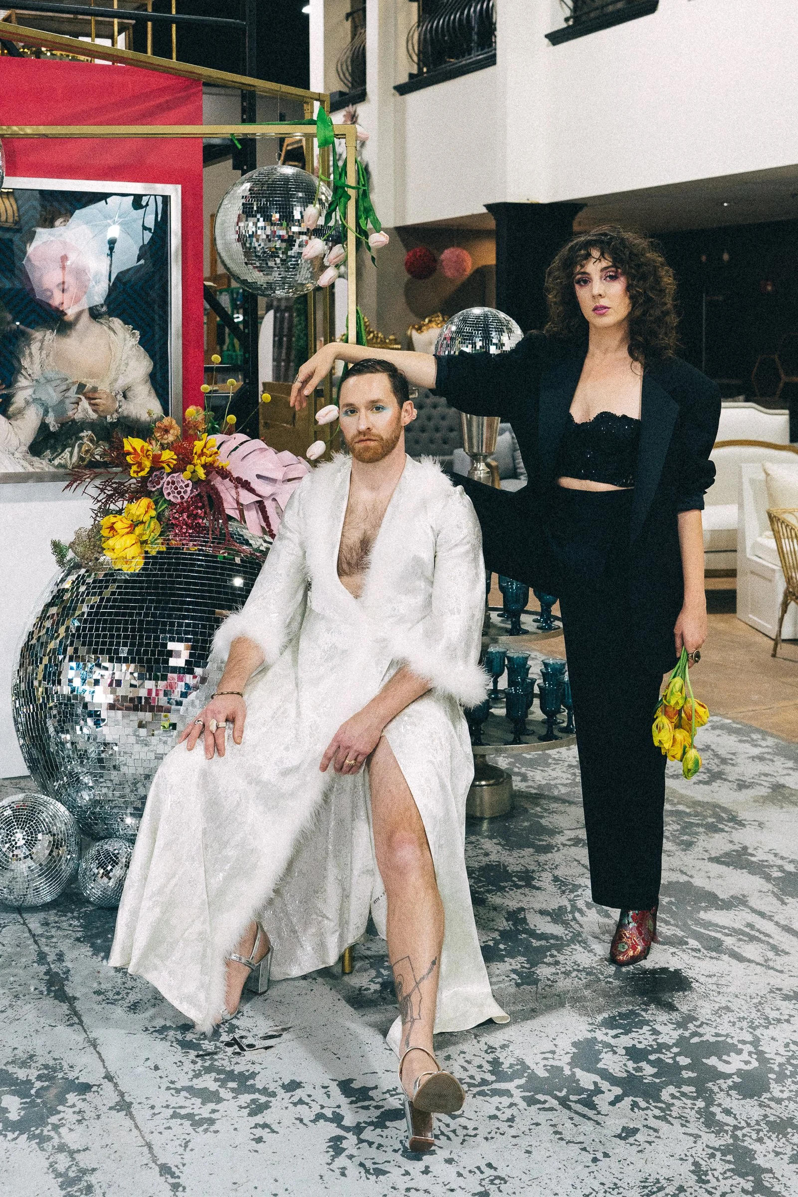 Two newlyweds pose in their wedding garb next to a giant disco ball.