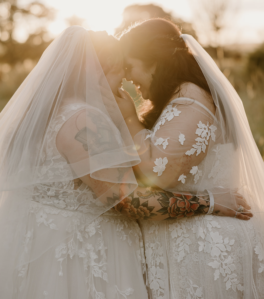 Sunlight steams down on two brides holding each other close at dusk.