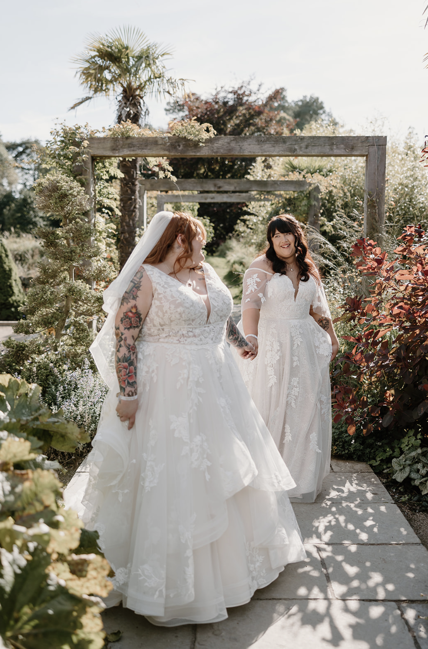 Two brides walk along holding hands and smiling with joy.