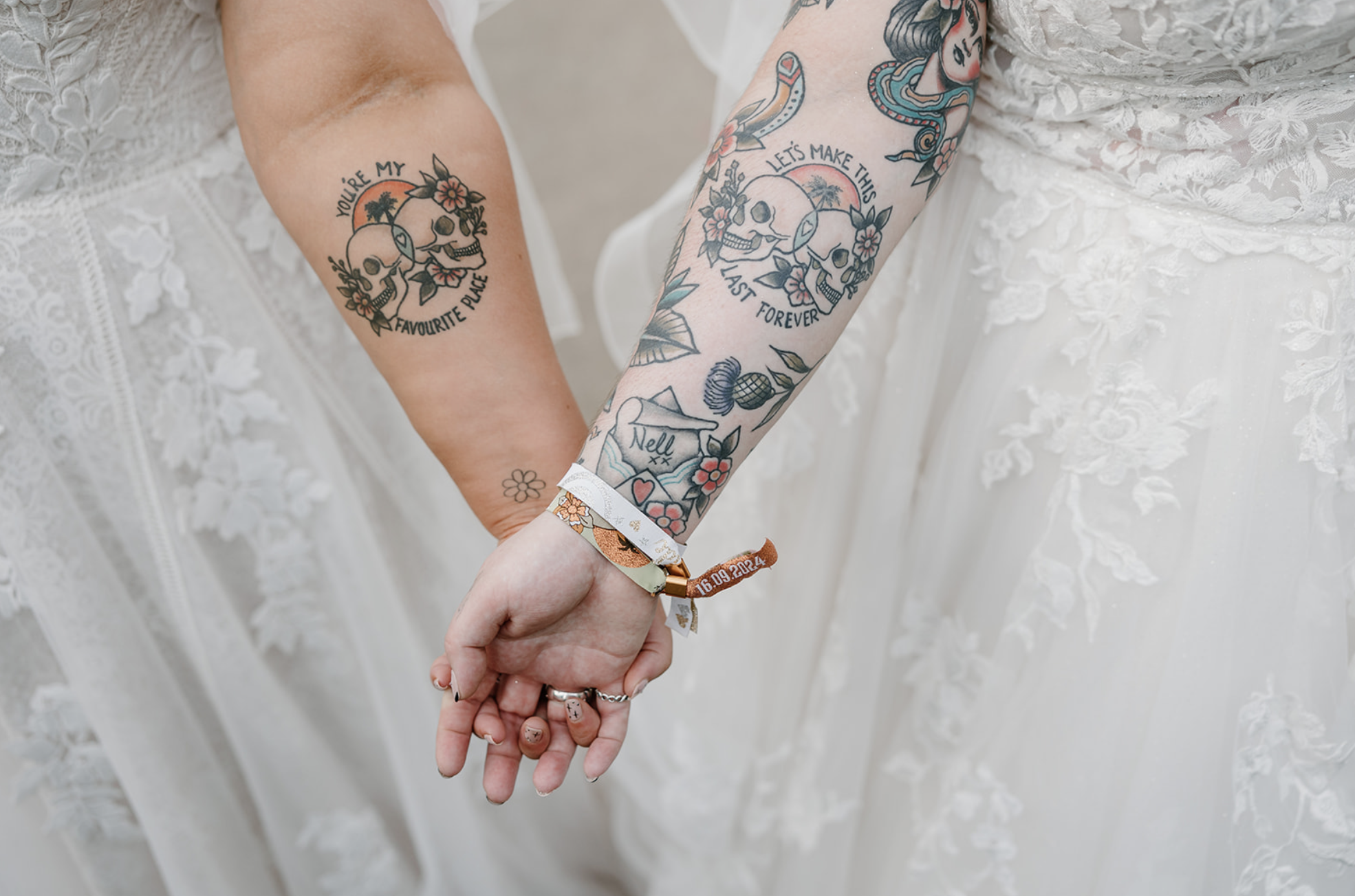 Two women hold their arms out to display their matching skull tattoos.