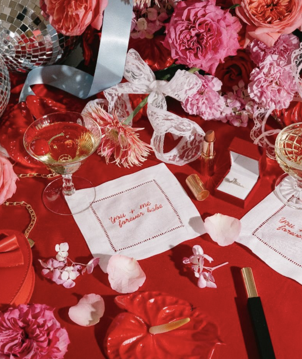 A table adorned with red and pink flowers, napkins, disco balls and champagne glasses.