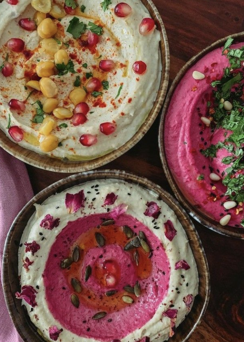 Three bowls of colourful organic dips with edible flowers and pomegranate seeds.