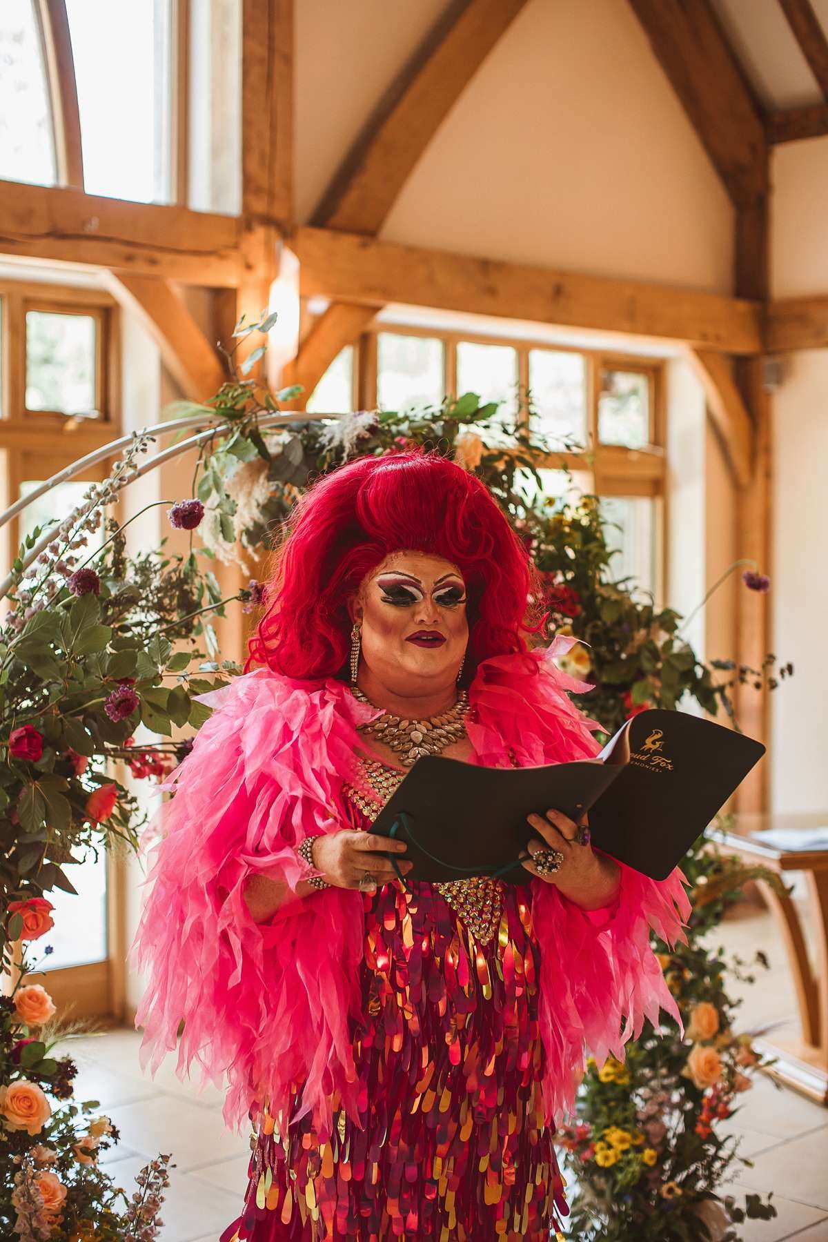 A draw queen with pink hair, pink coat and pink sequinned dress delivers a wedding ceremony.